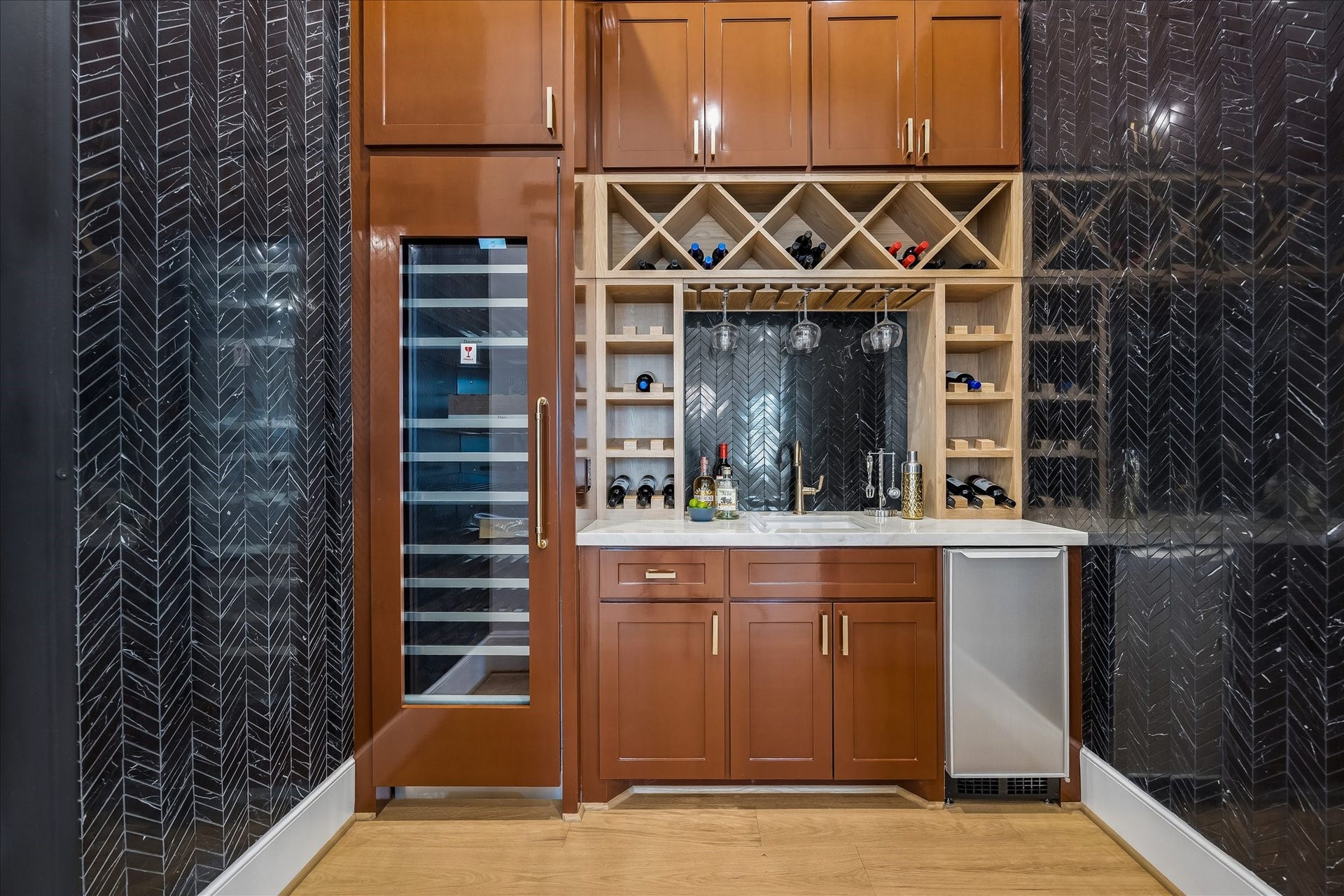 Dedicated wine room makes a statement with dramatic herringbone tile, temperature controlled wine storage and custom bottle and stemware racks. A built in sink, beverage refrigerator and extensive cabinetry create a polished space for serving and entertaining.