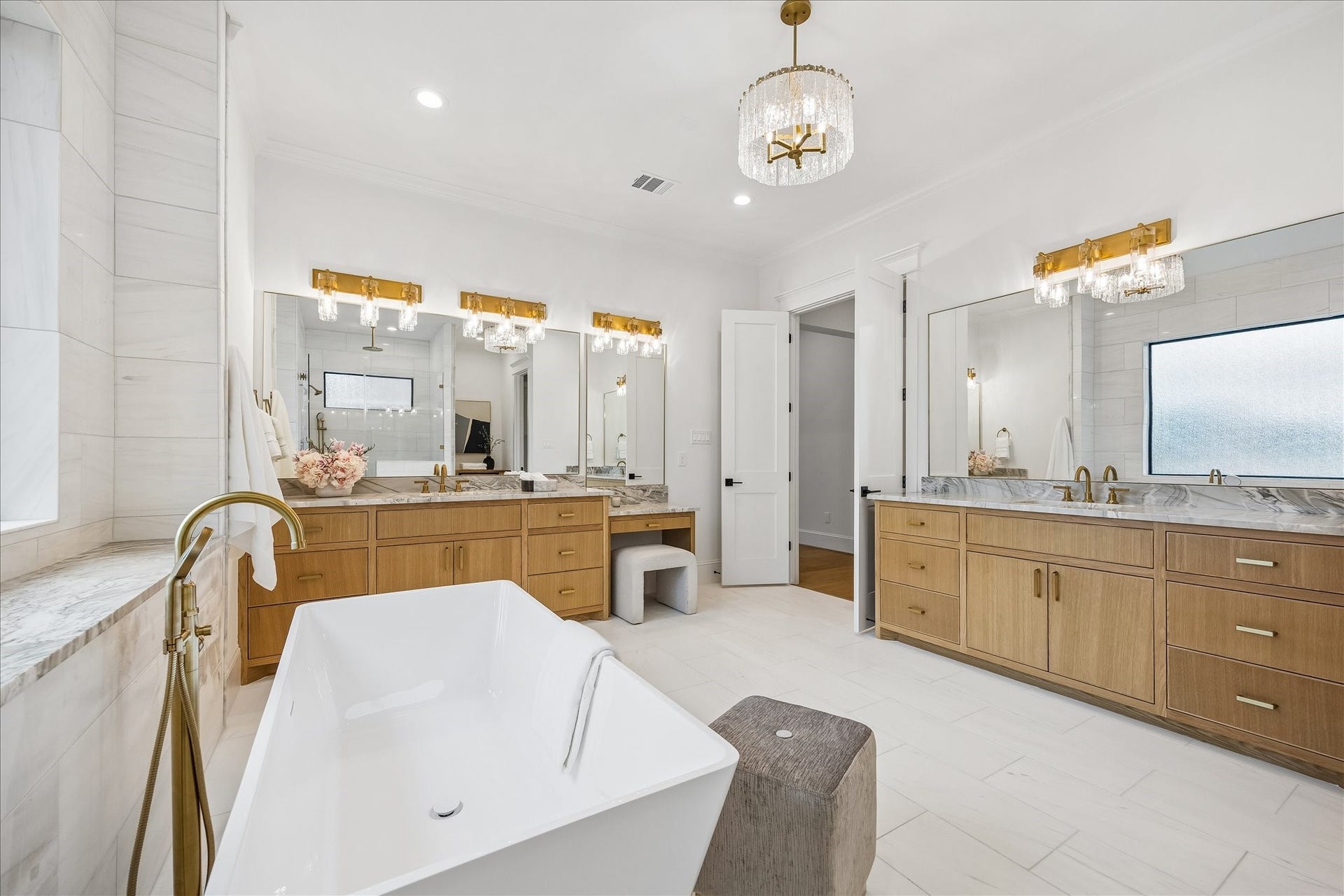 Separate vanities provide exceptional counter space and storage, complemented by natural wood cabinetry, granite countertops and statement brass lighting. A dedicated vanity area adds another thoughtful detail to the primary bath.