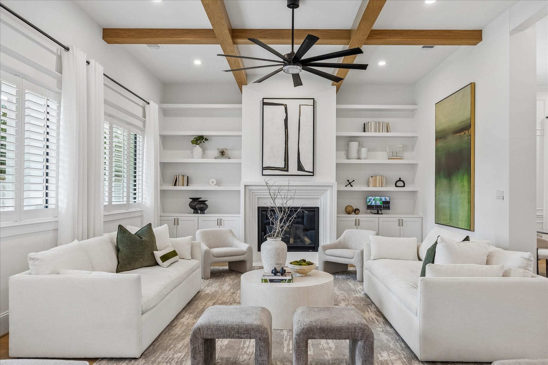 Custom built ins frame the fireplace, while a coffered ceiling with natural wood beams adds warmth and architectural dimension. Plantation shutters bring filtered natural light into the living space.