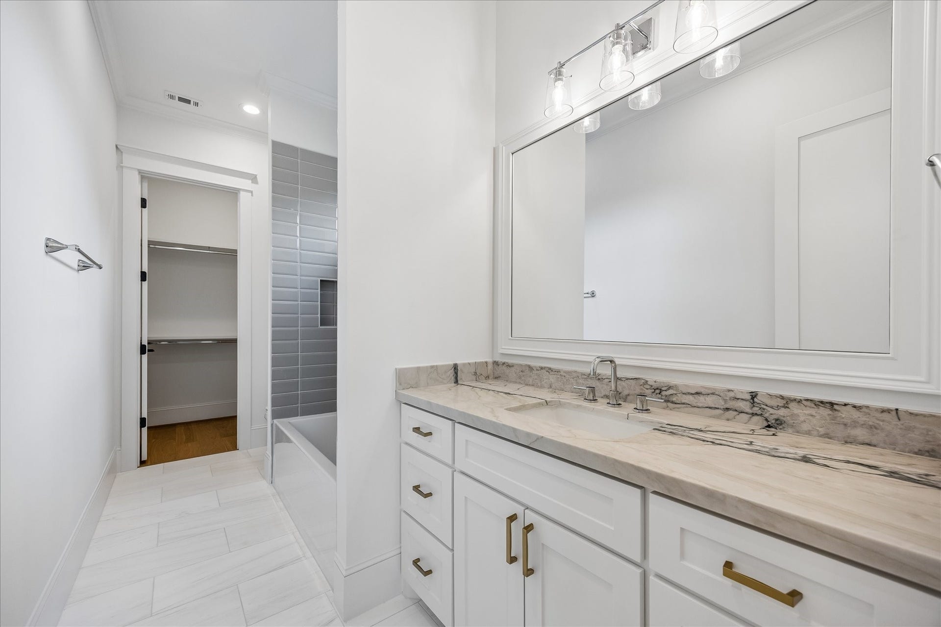 Ensuite bath pairs a granite countertop with crisp white cabinetry, brass hardware and a tiled tub and shower surround. Direct access to the walk in closet keeps the suite thoughtfully connected.