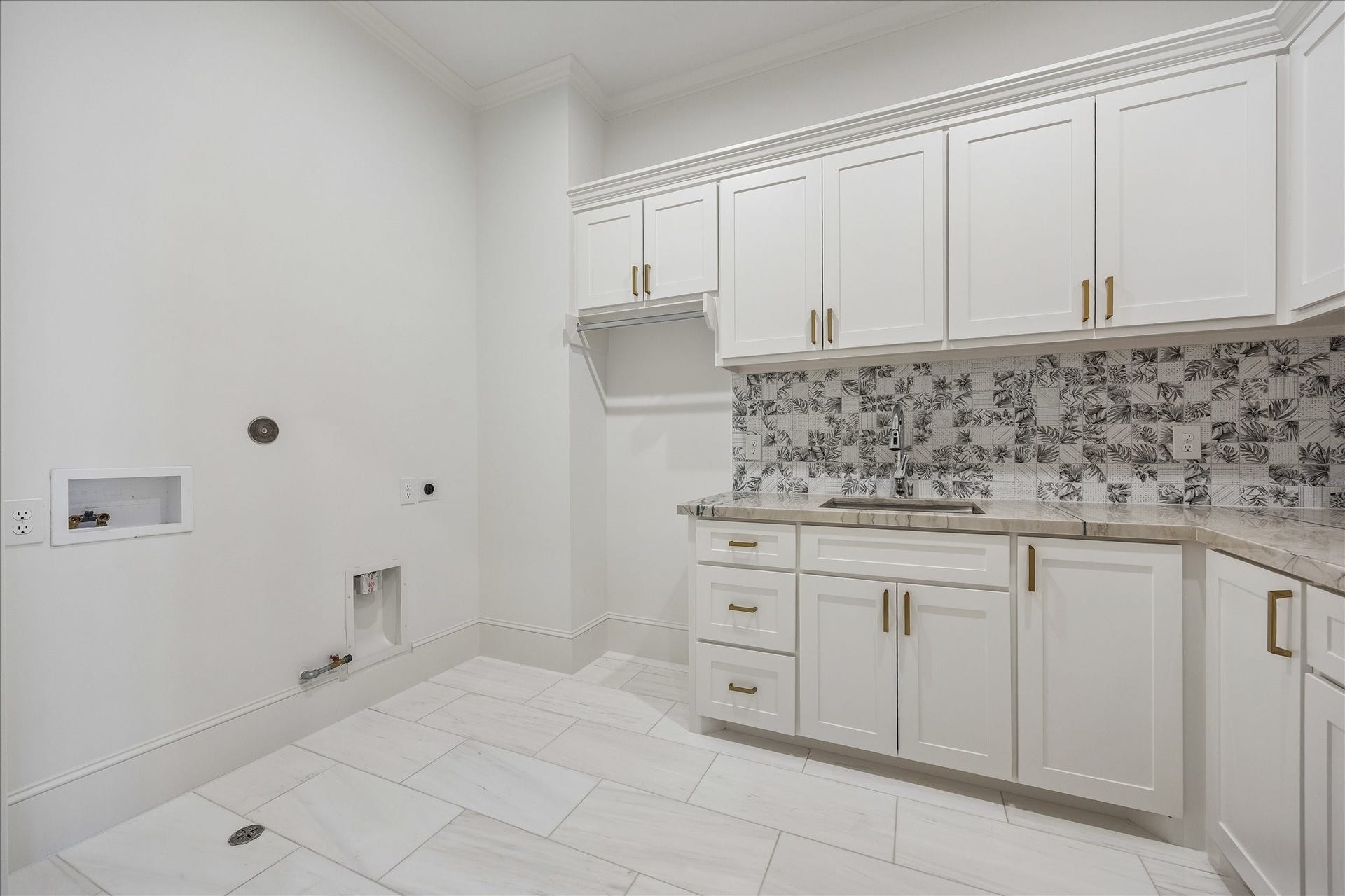 Spacious utility room pairs extensive cabinetry with a stone countertop, sink and hanging space, creating a well organized home base for laundry and everyday storage.