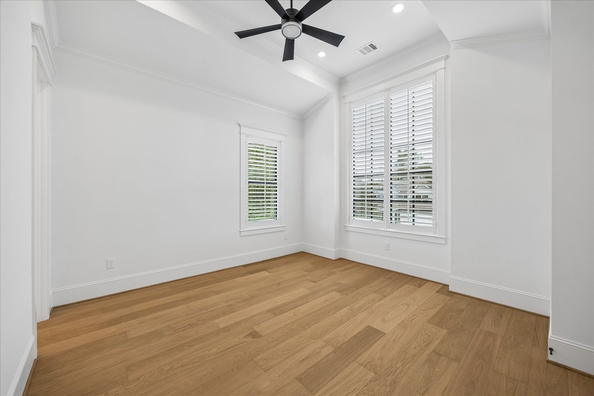 Bright secondary bedroom features a tray ceiling, wide plank wood flooring and windows on two walls for abundant natural light. Generous proportions leave plenty of flexibility for a comfortable bedroom setup.