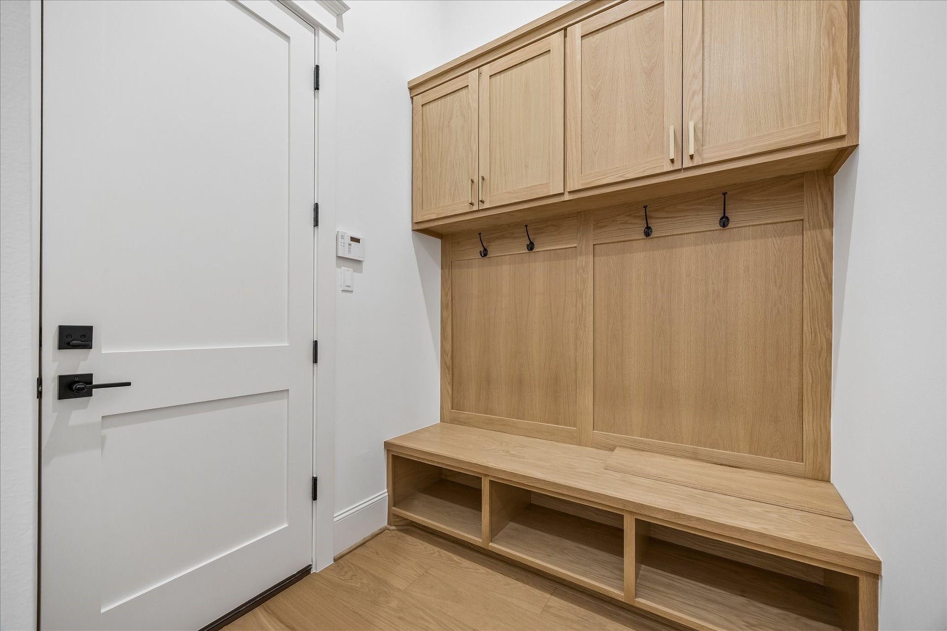 Custom mudroom keeps daily routines organized with a built in bench, open shoe storage, hooks and overhead cabinetry positioned just inside the exterior entry.