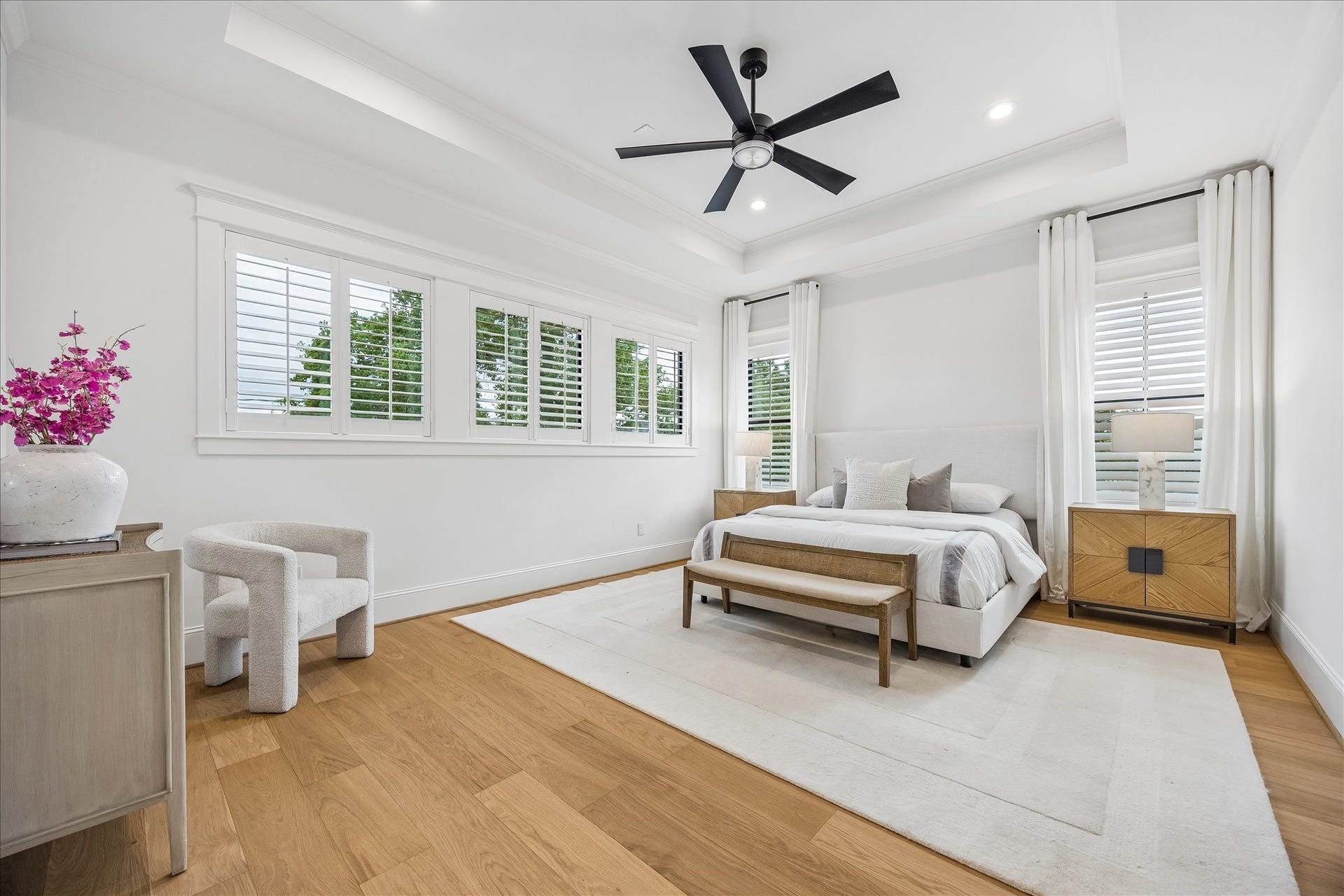 Spacious primary suite is wrapped in natural light from multiple windows and finished with a tray ceiling, wide plank wood flooring and generous proportions for a private retreat.