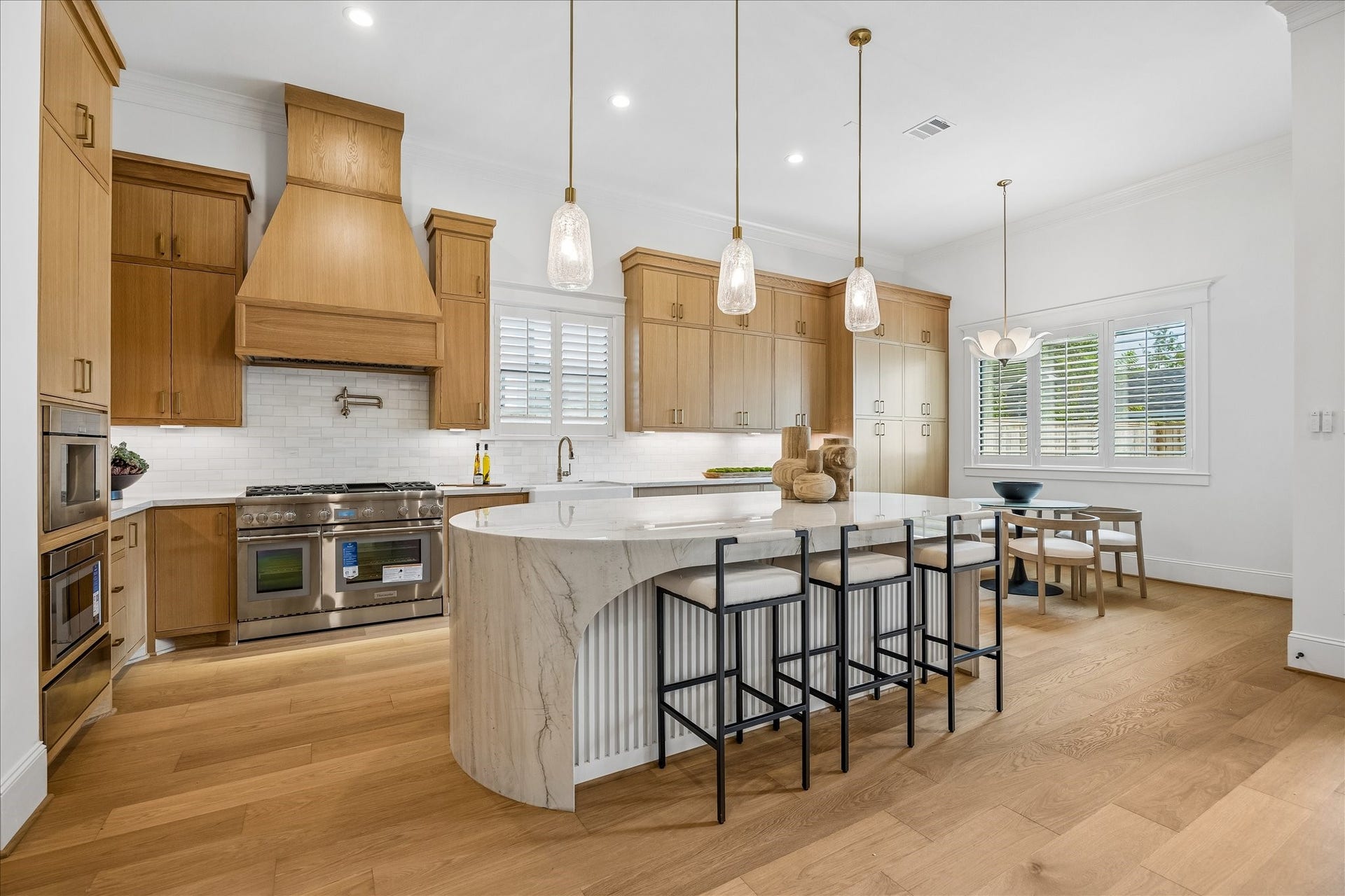 Expansive kitchen combines generous prep and storage space with a large central island and adjacent breakfast area. Plantation shutters, wide plank hardwood floors and layered natural wood finishes carry the homes refined design into the heart of the home.