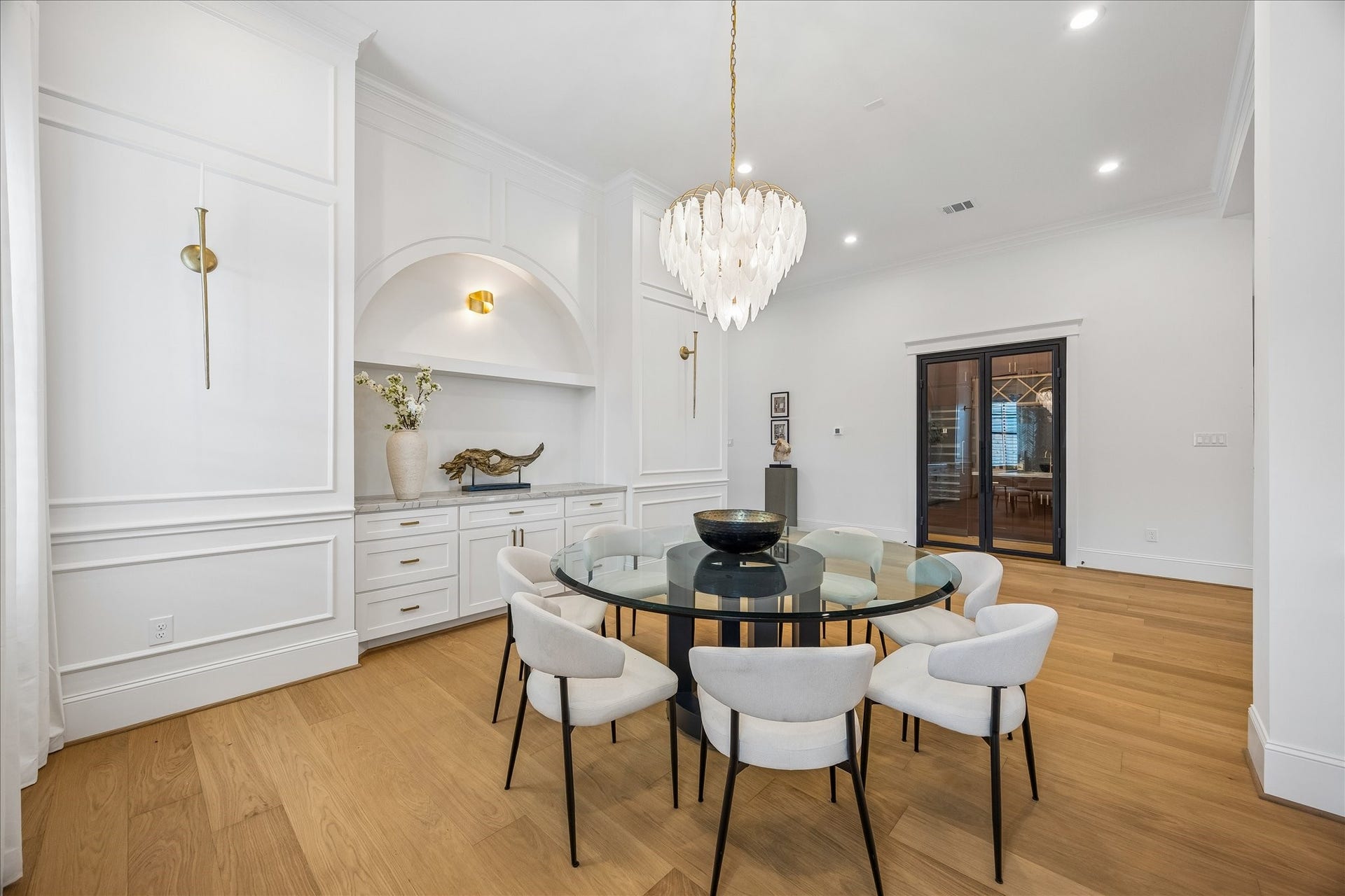 Formal dining is elevated by extensive custom millwork, integrated cabinetry and an arched niche with a stone countertop. Glass doors lead directly to the adjacent wine room, creating a thoughtful setup for entertaining.