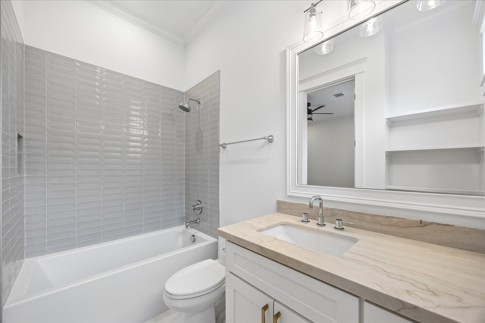 Private ensuite bath features built in shelving and a tub and shower combination finished with sleek gray tile.