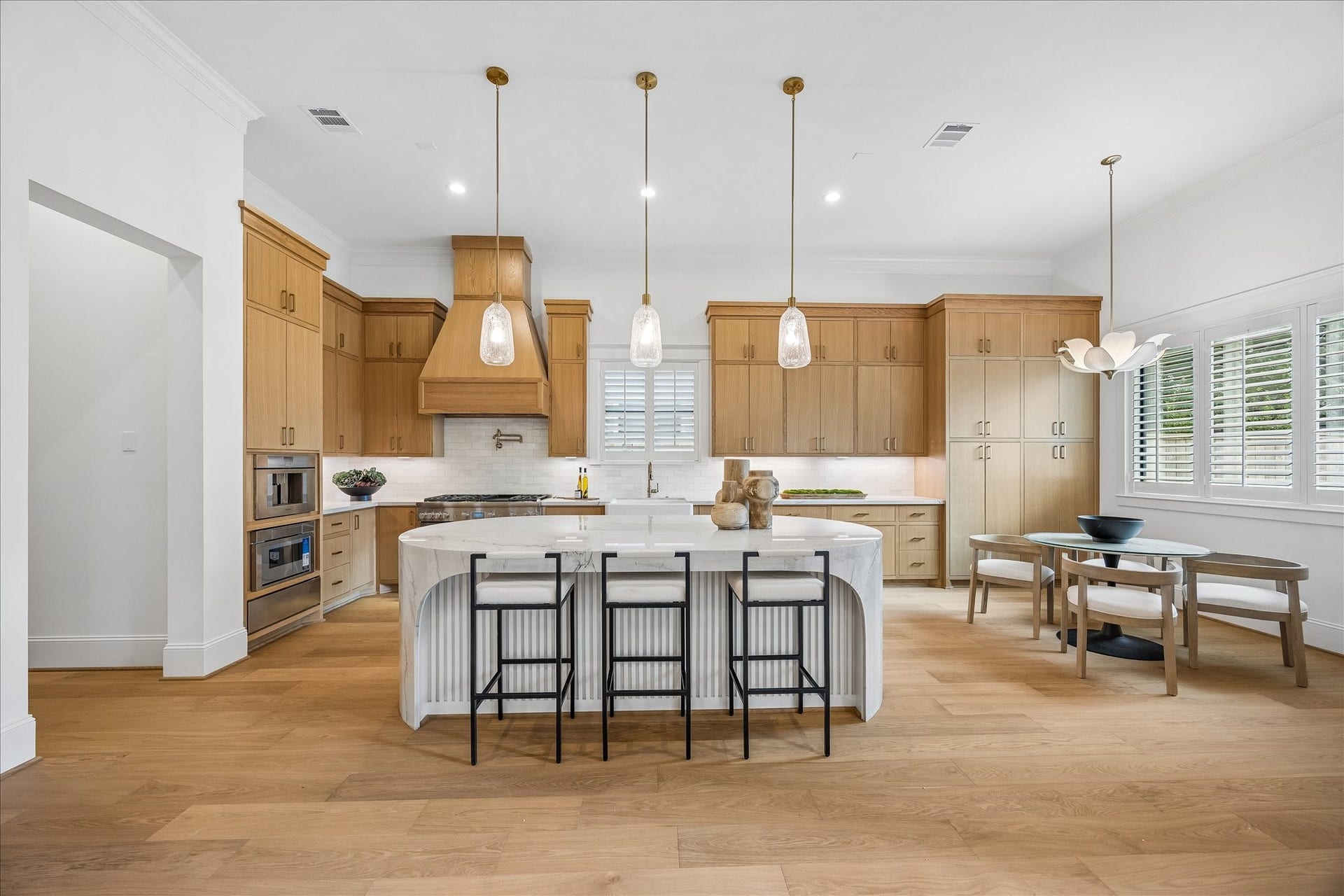 Warm wood cabinetry extends to the ceiling, complemented by a statement wood vent hood, granite countertops and an oversized waterfall island with sculpted detailing. Extensive cabinetry and professional style appliances balance elevated design with everyday functionality.