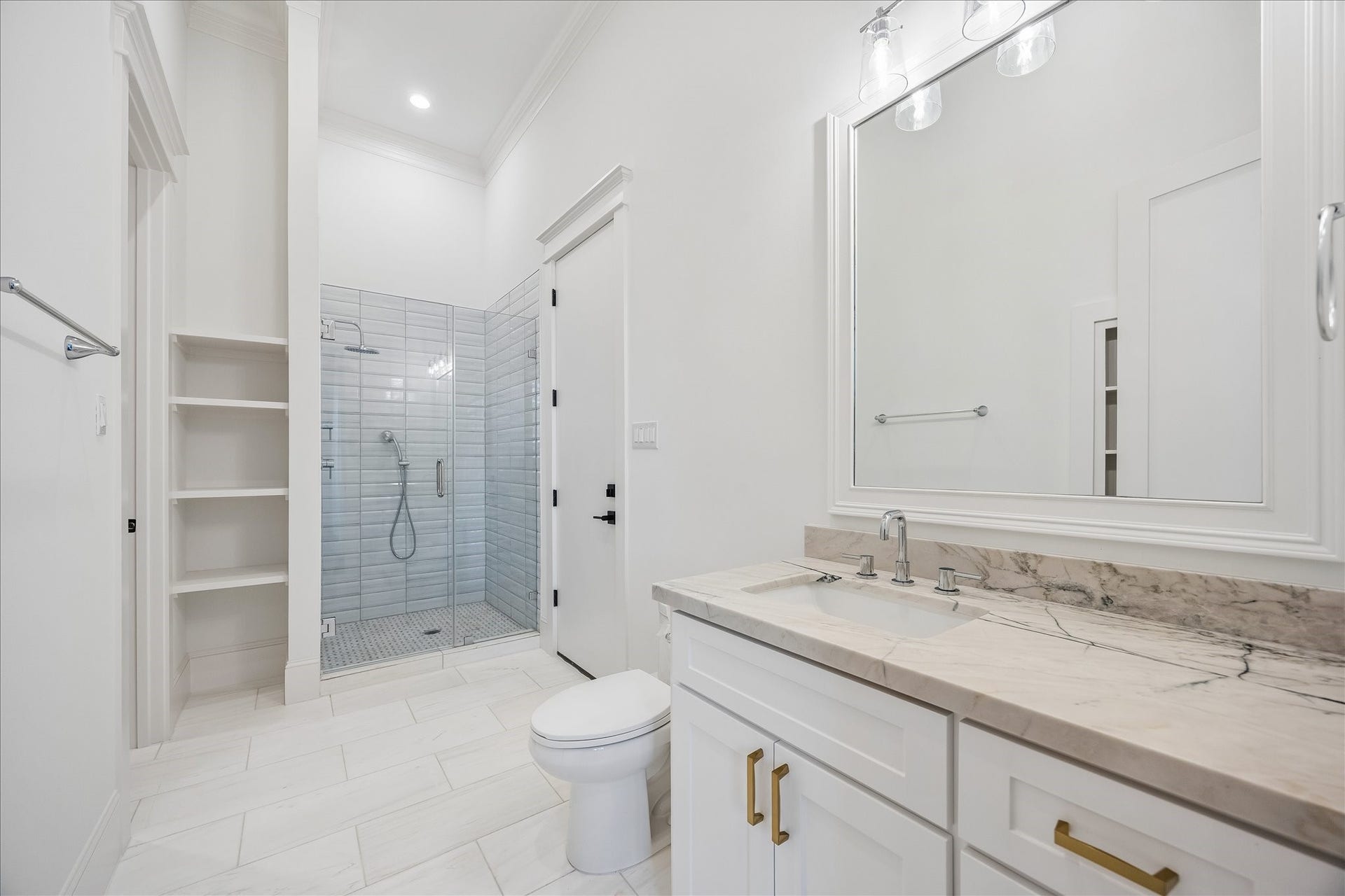 Private ensuite serving the study or fifth bedroom features a granite topped vanity, brass hardware, built in shelving and a glass enclosed shower finished in soft gray tile.