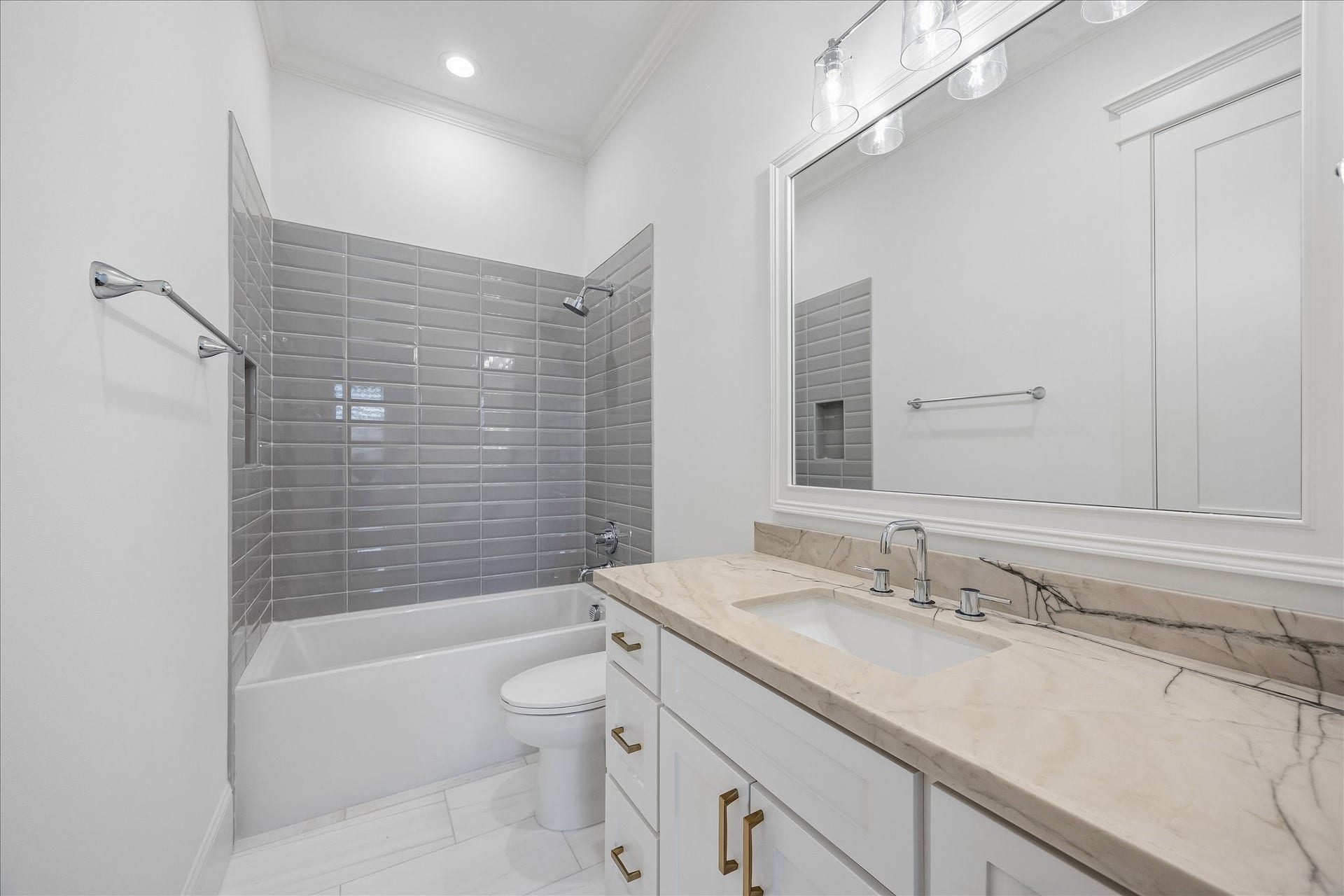 Ensuite bath continues the clean, refined finishes with a granite vanity, brass hardware and a tub and shower combination wrapped in glossy gray tile.