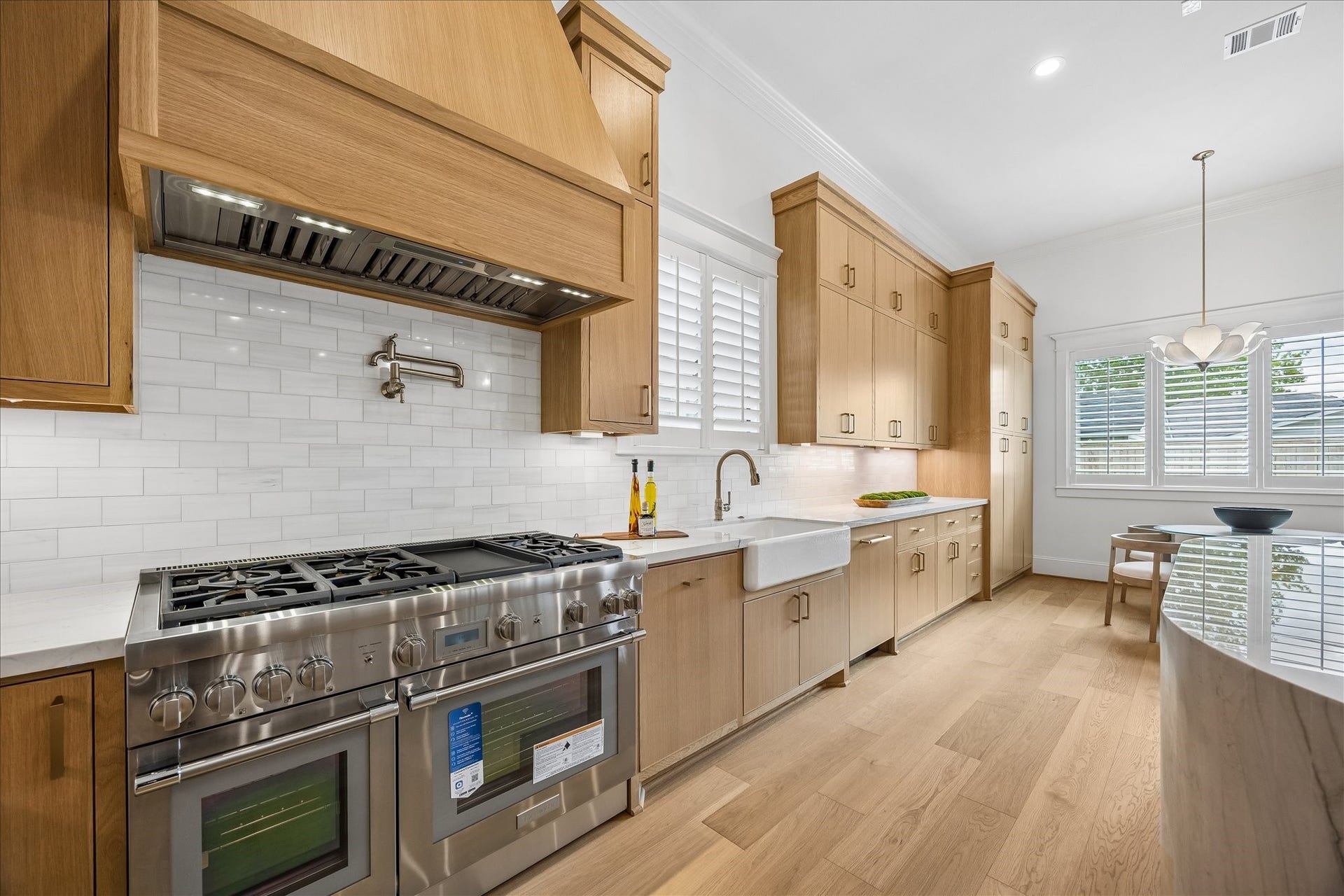 Professional style Thermador double gas range sits beneath a custom wood vent hood with a pot filler and tile backsplash. Floor to ceiling cabinetry, a farmhouse sink and abundant prep space balance elevated design with everyday practicality.