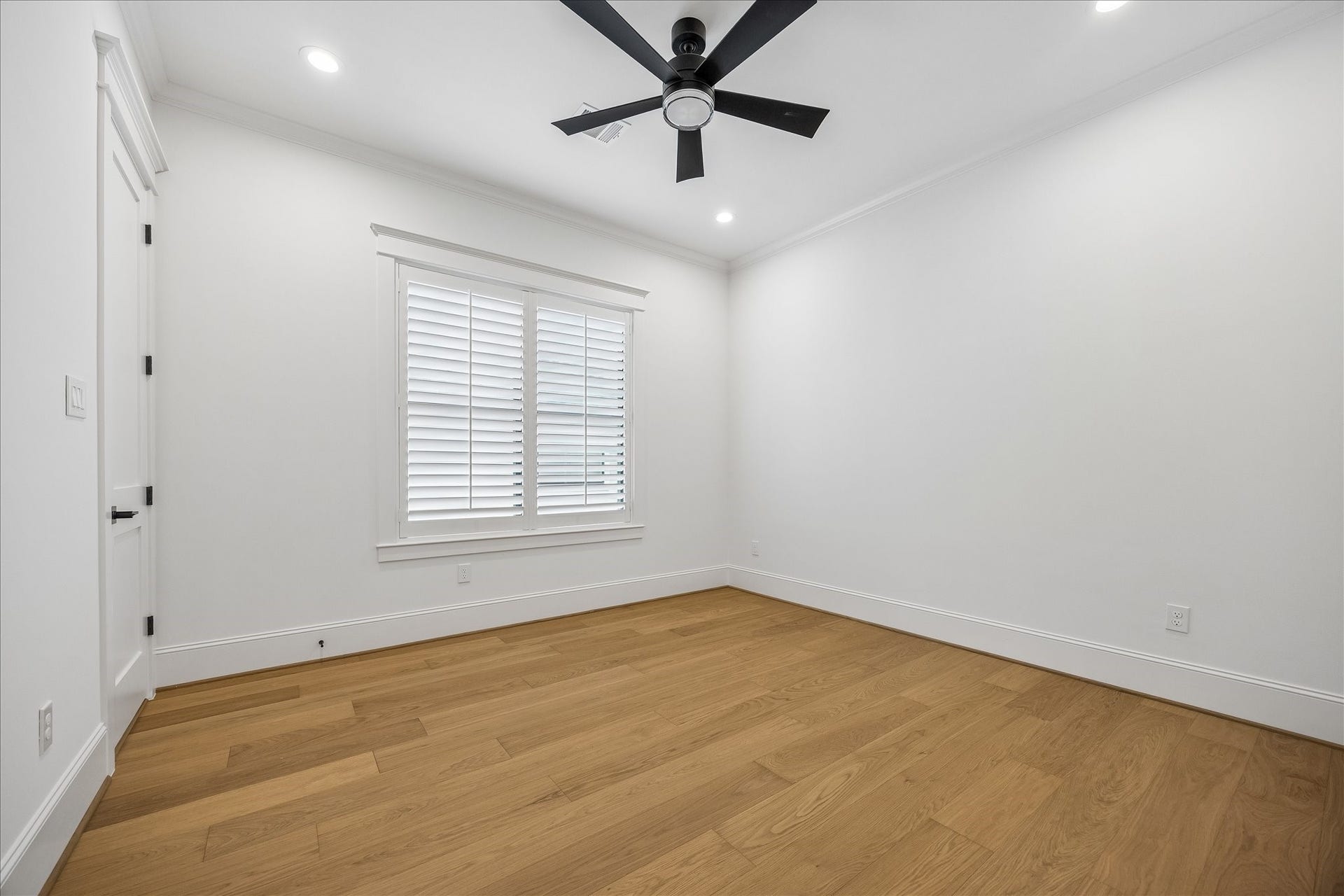 Bright secondary bedroom pairs hardwood flooring with a high ceiling, recessed lighting and a shuttered window for natural light and privacy.