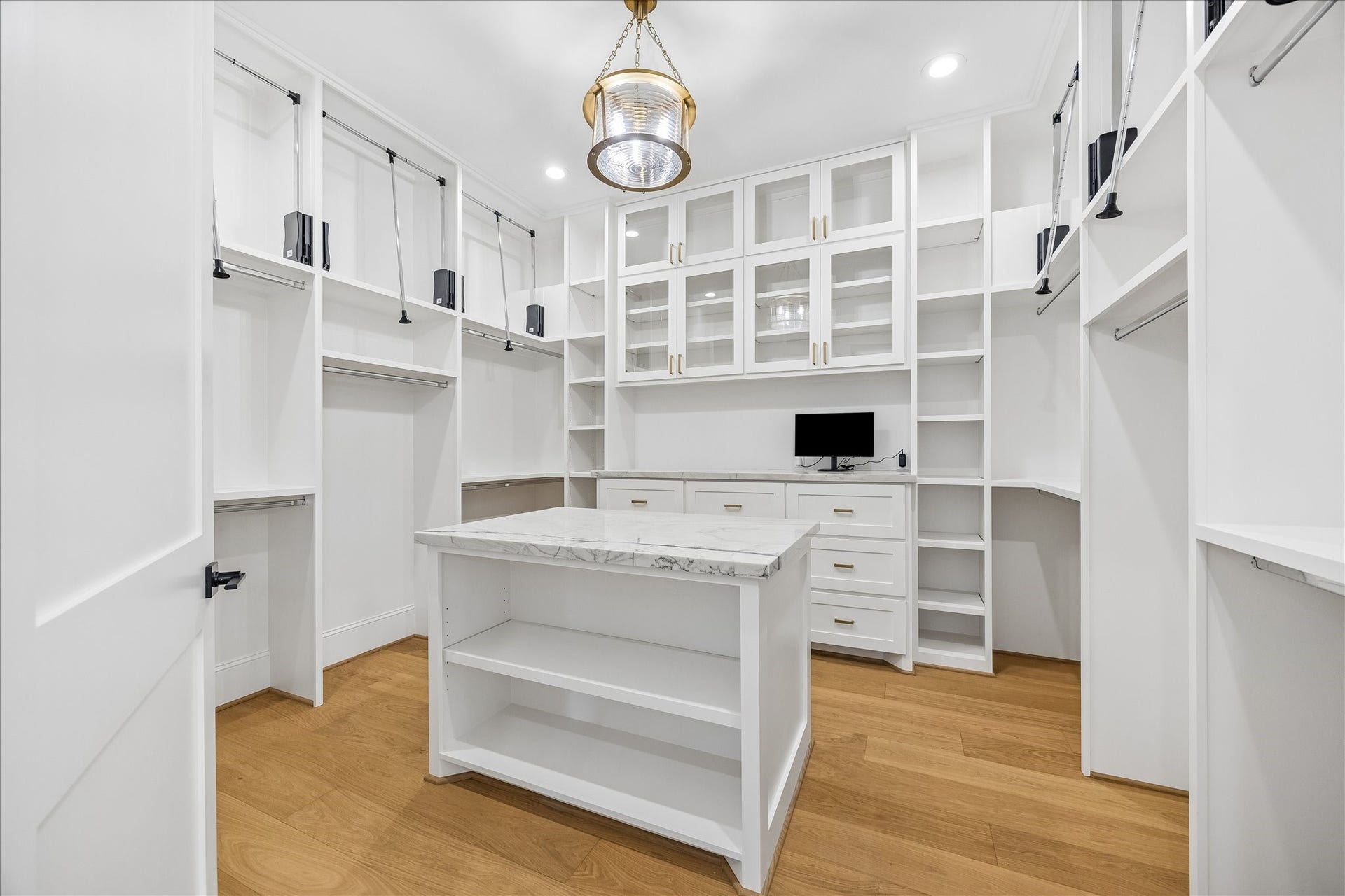 Custom primary closet is thoughtfully designed with floor to ceiling built ins, extensive hanging space, glass front cabinetry and a stone topped center island. Integrated drawers, shelving and dedicated counter space create an exceptionally organized dressing area.