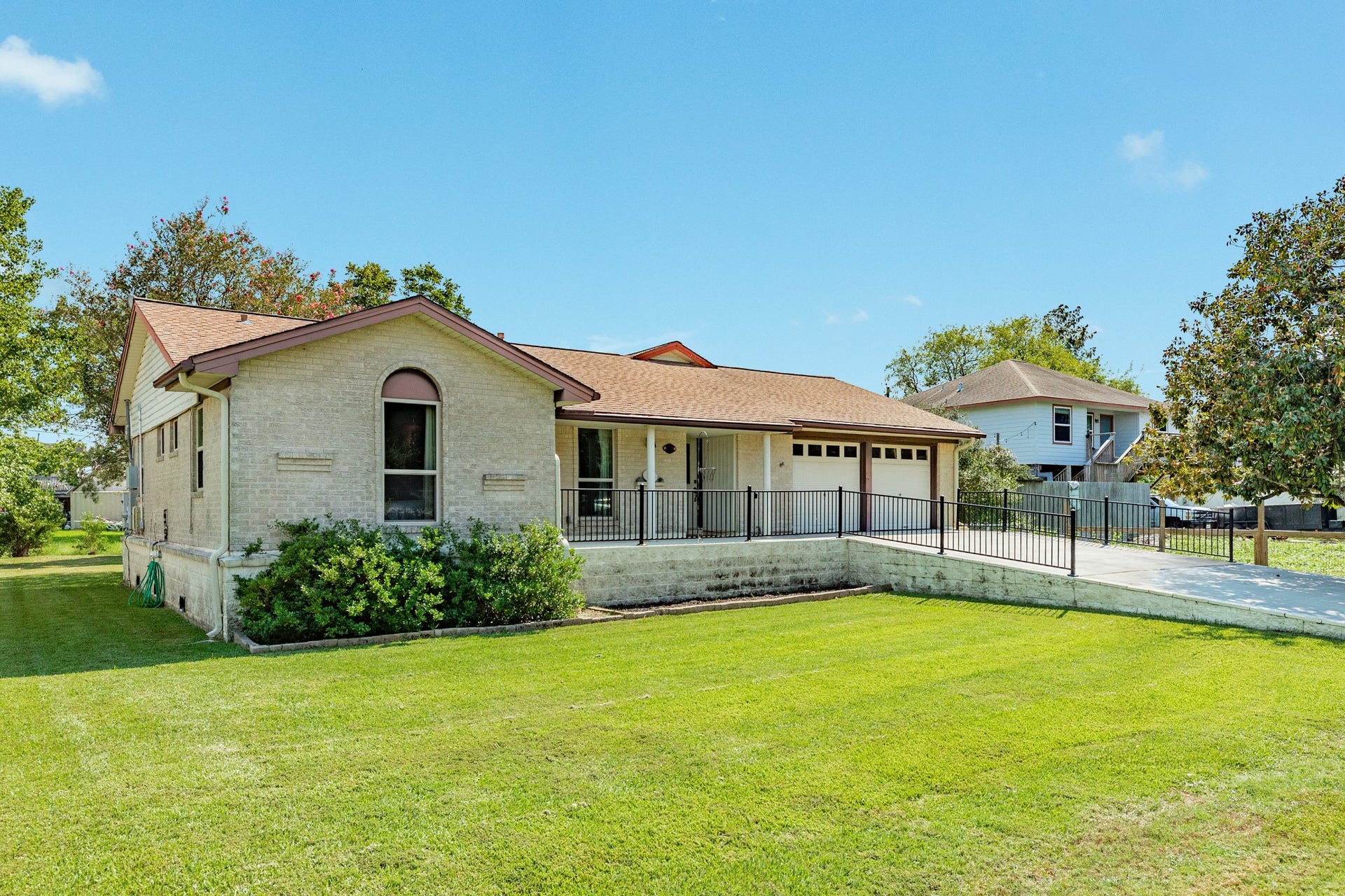Single-story home with a light brick exterior has been raised 40 inches for peace of mind during flooding events. A spacious concrete driveway leads to the attached two-car garage and covered front porch. The generous covered entry provides a welcoming approach to the home and features a decorative glass front door.