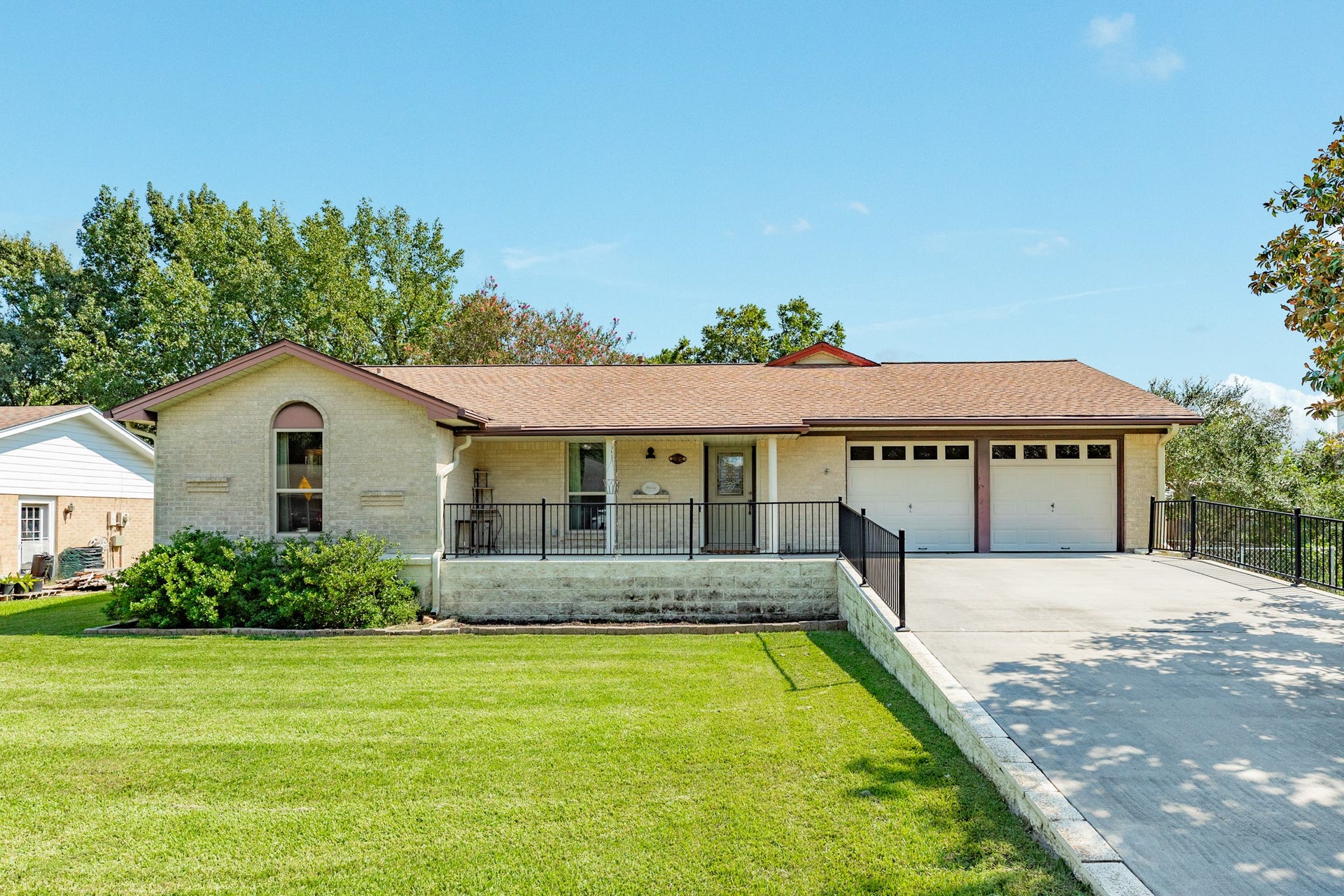 Single-story home with a light brick exterior has been raised 40 inches for peace of mind during flooding events. A spacious concrete driveway leads to the attached two-car garage and covered front porch. The generous covered entry provides a welcoming approach to the home and features a decorative glass front door.