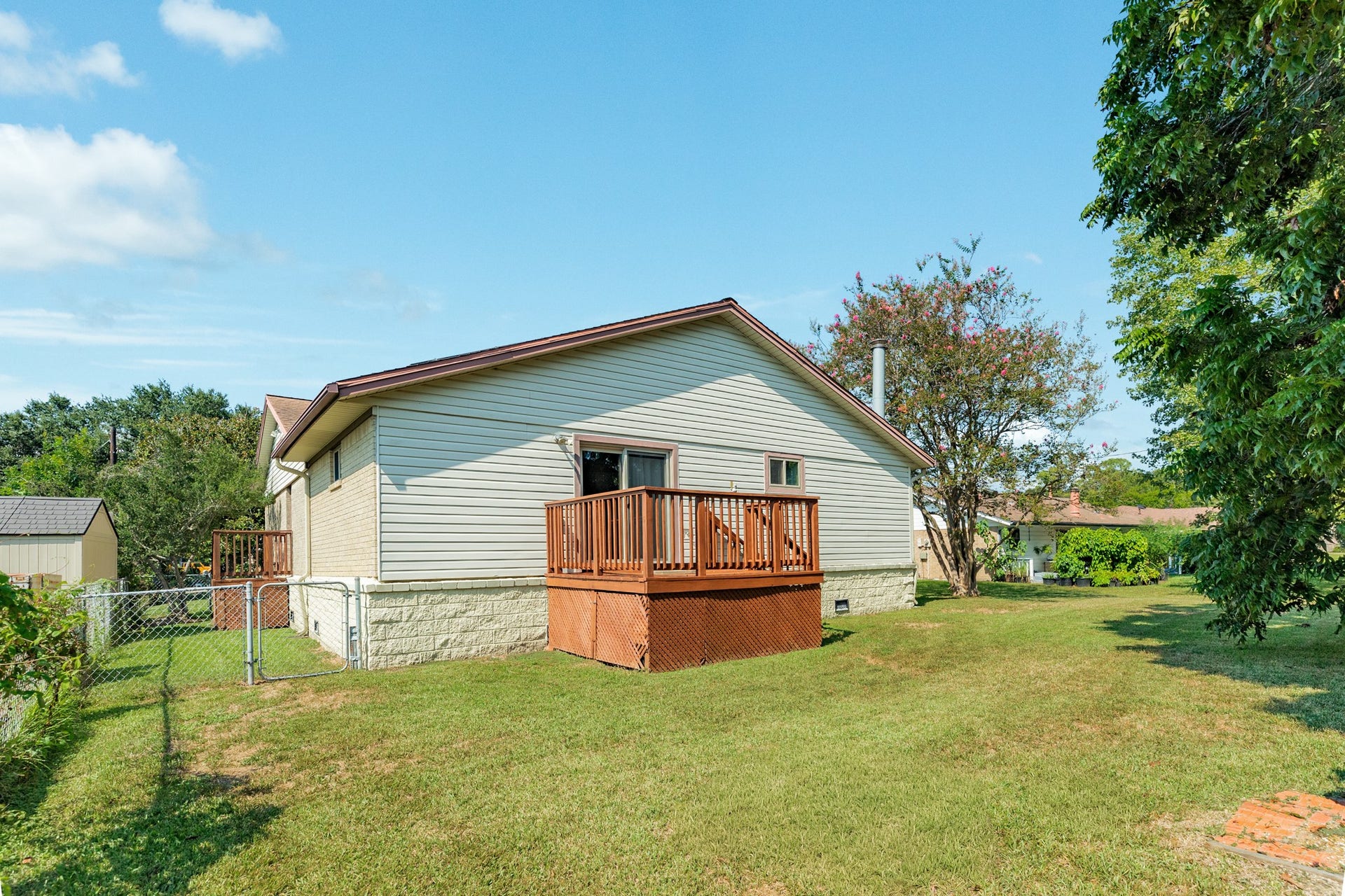 Spacious backyard provides abundant green space surrounded by mature trees, offering plenty of room for outdoor activities, gardening, or entertaining. A raised wood deck with stairs overlooks the yard and creates a convenient outdoor gathering space directly accessible from the home.