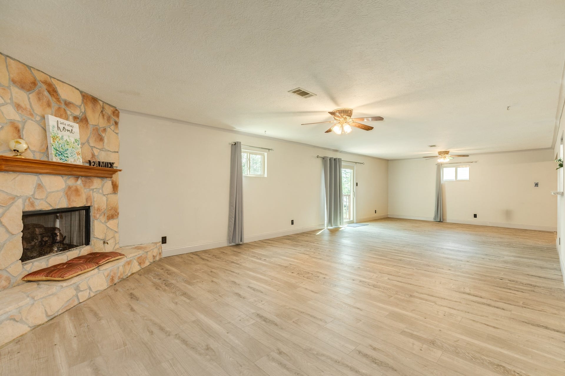 Impressively spacious family room provides an exceptional second living area highlighted by a floor-to-ceiling stone fireplace with raised hearth and wood mantel. Abundant wall space, and wood-look flooring enhance the expansive layout, while windows and a sliding glass door bring in natural light and provide direct access to the backyard deck.