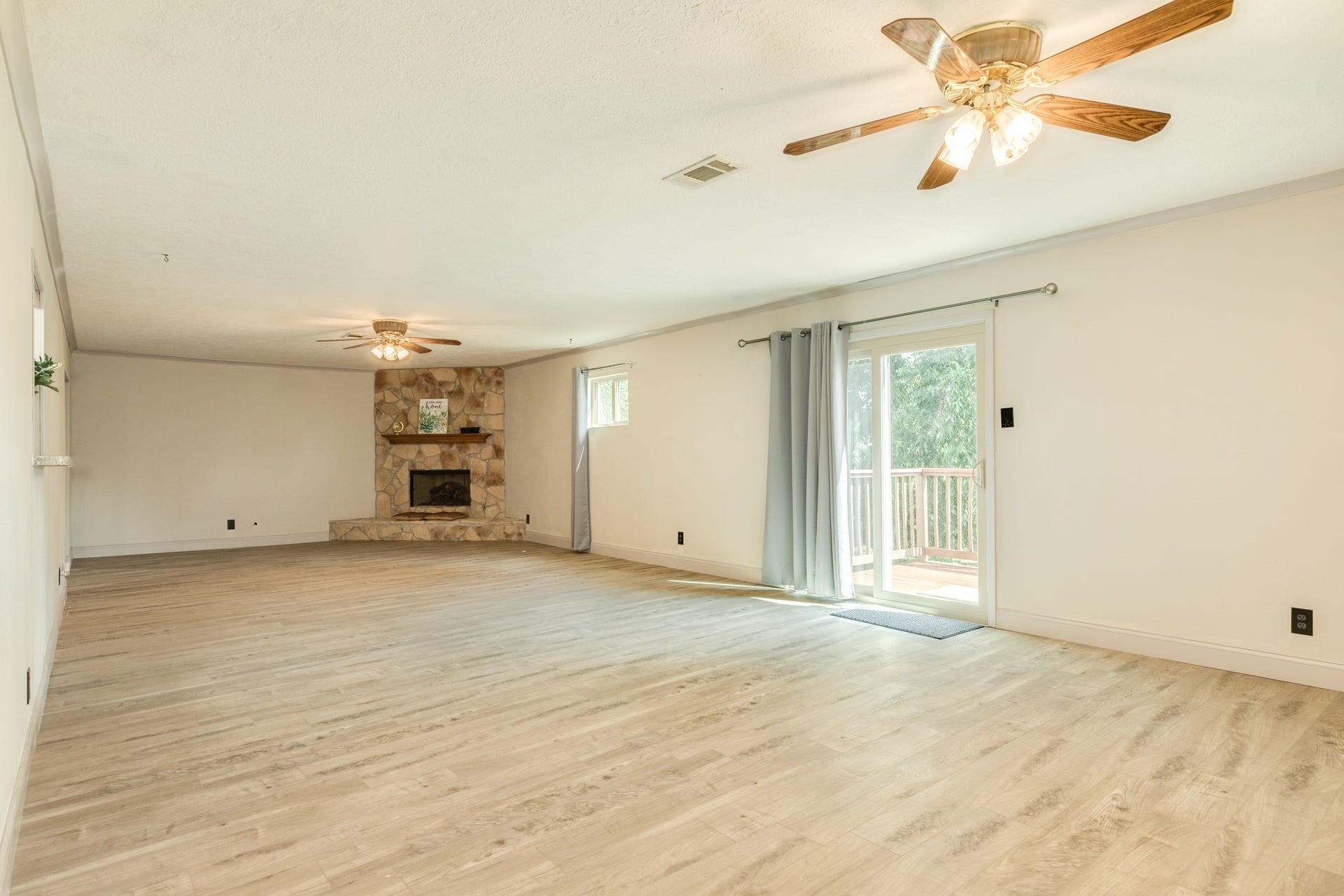Impressively spacious family room provides an exceptional second living area highlighted by a floor-to-ceiling stone fireplace with raised hearth and wood mantel. Abundant wall space, and wood-look flooring enhance the expansive layout, while windows and a sliding glass door bring in natural light and provide direct access to the backyard deck.