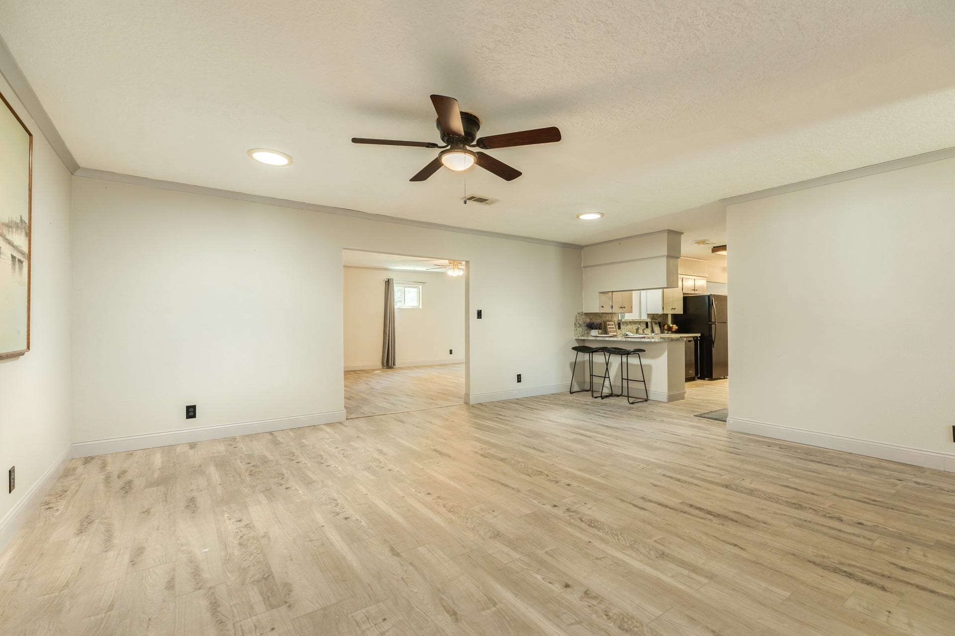 Spacious living room adjacent to the kitchen offers an open, versatile layout with attractive wood-look flooring, neutral finishes, recessed lighting. The generous footprint provides plenty of flexibility for multiple furniture arrangements, while the open connection to the kitchen and adjoining living spaces creates an easy flow for everyday living and entertaining.