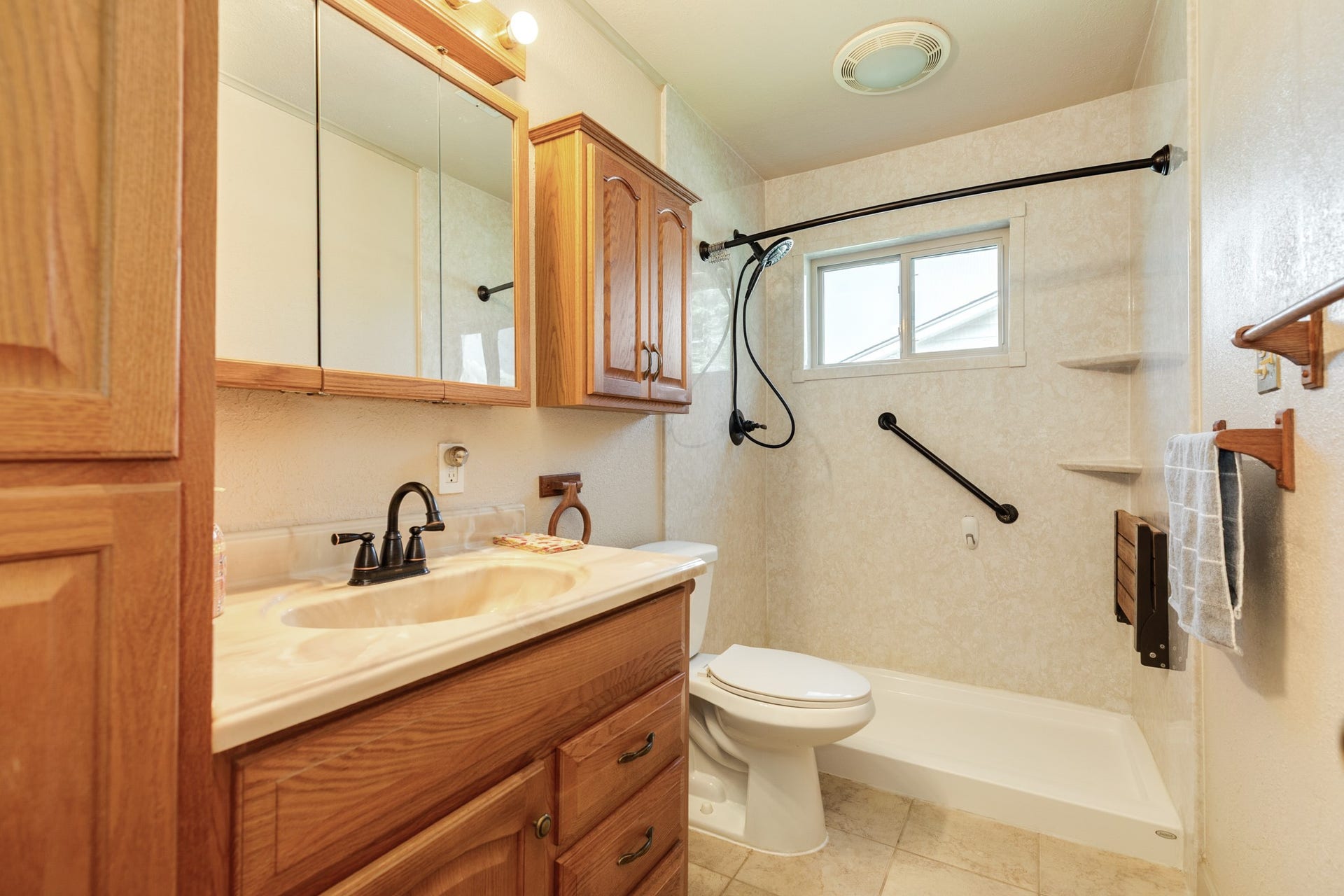 Full bath with wood cabinetry and additional storage, combination tub/shower combination with surround, built-in corner shelving, window, and grab bar.