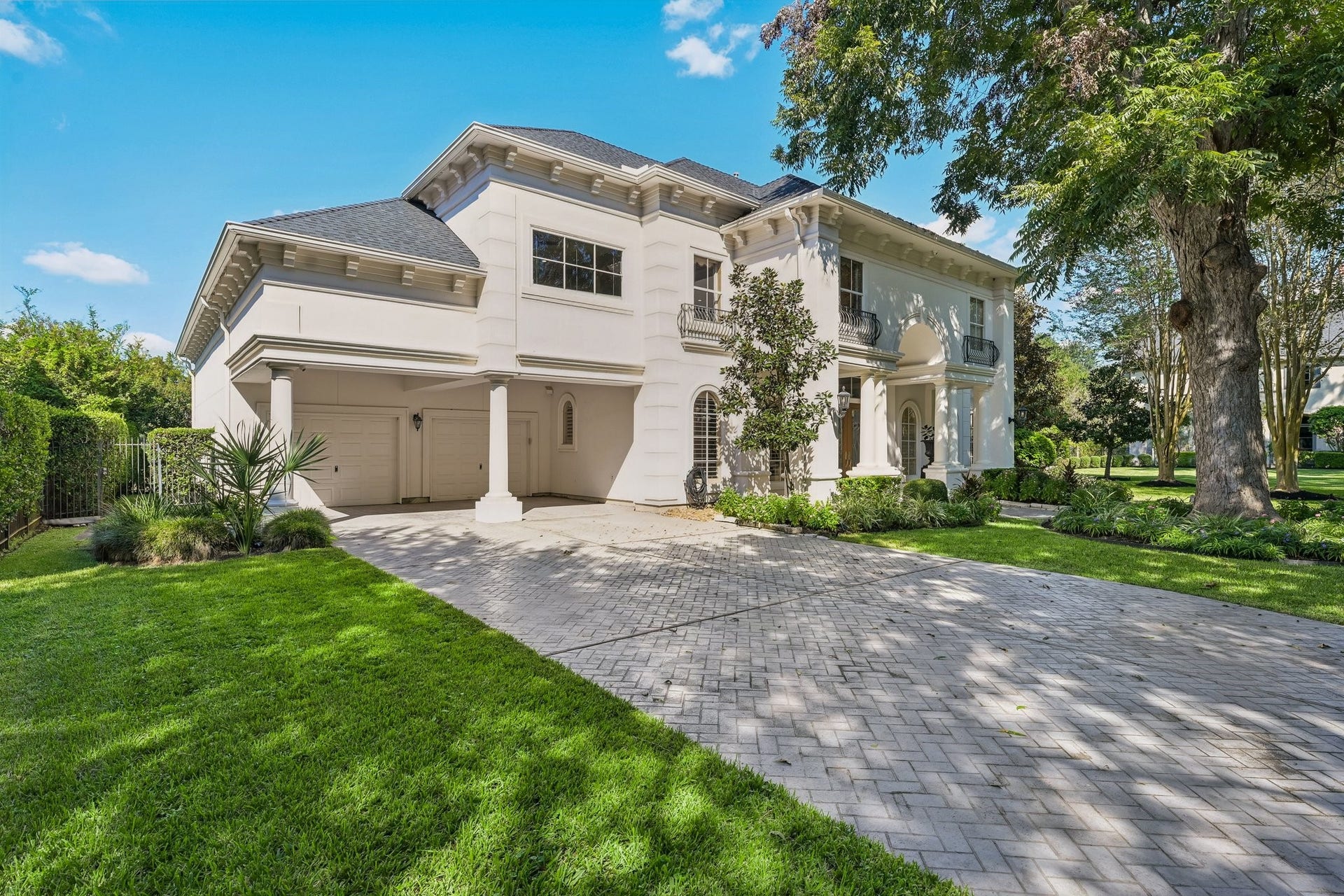 Elegant custom residence showcasing a spacious double-wide paver driveway, covered attached carport, and beautifully landscaped grounds framed by mature trees