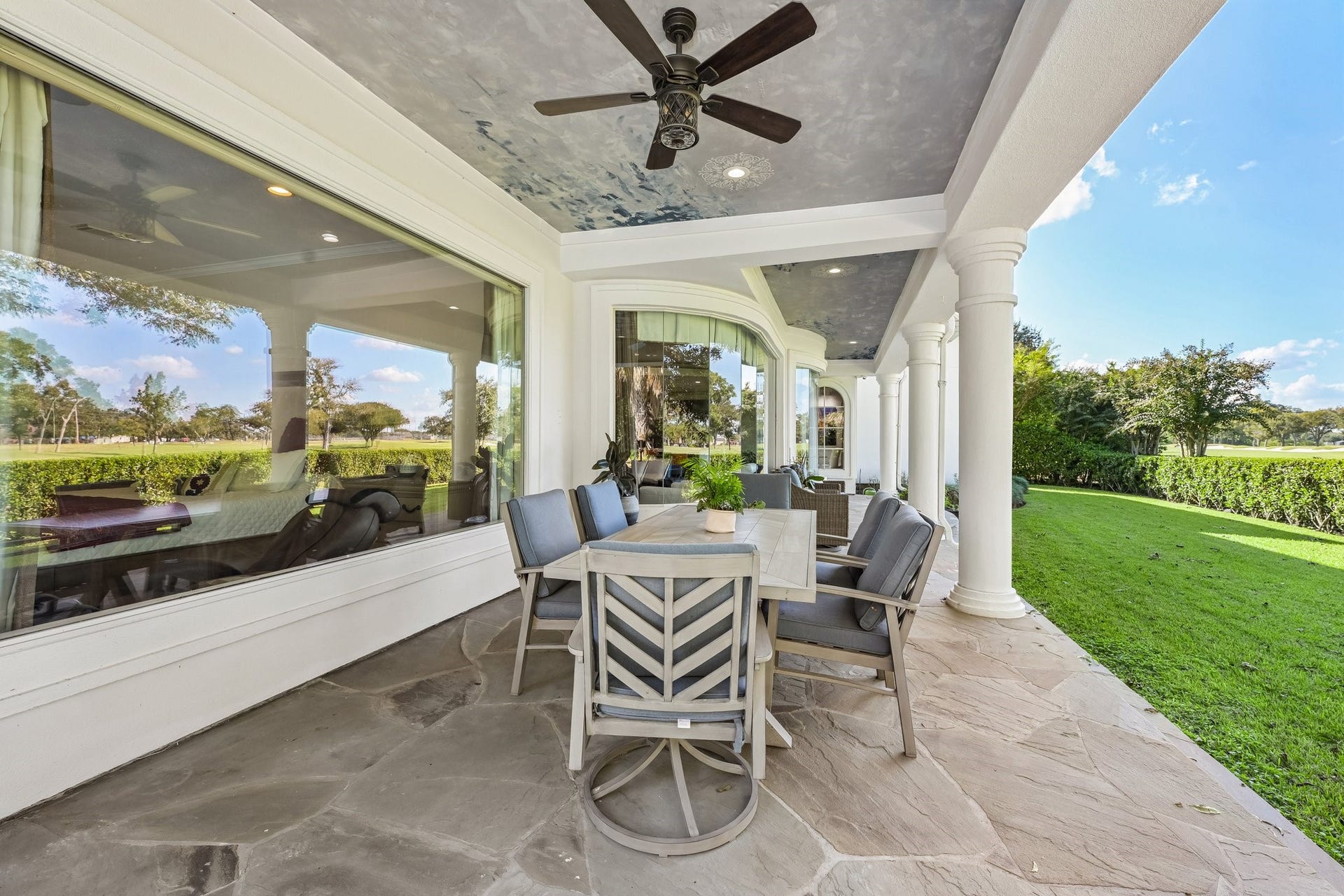 Expansive covered patio featuring an outdoor dining area, stone flooring, and elegant column details, creating an ideal setting for entertaining and enjoying the lush backyard