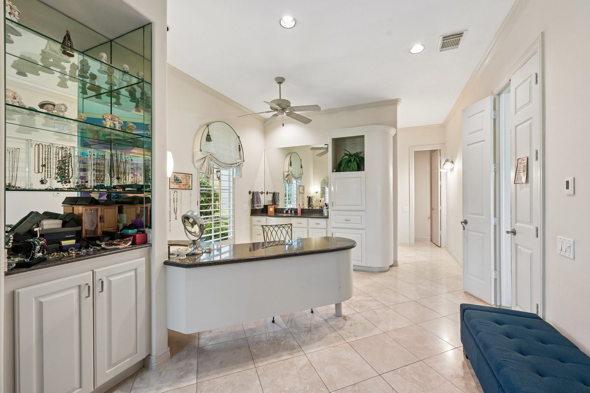 Well-appointed primary bathroom featuring dual sinks, an extended vanity with a dark stone countertop, and custom glass-front display cabinetry