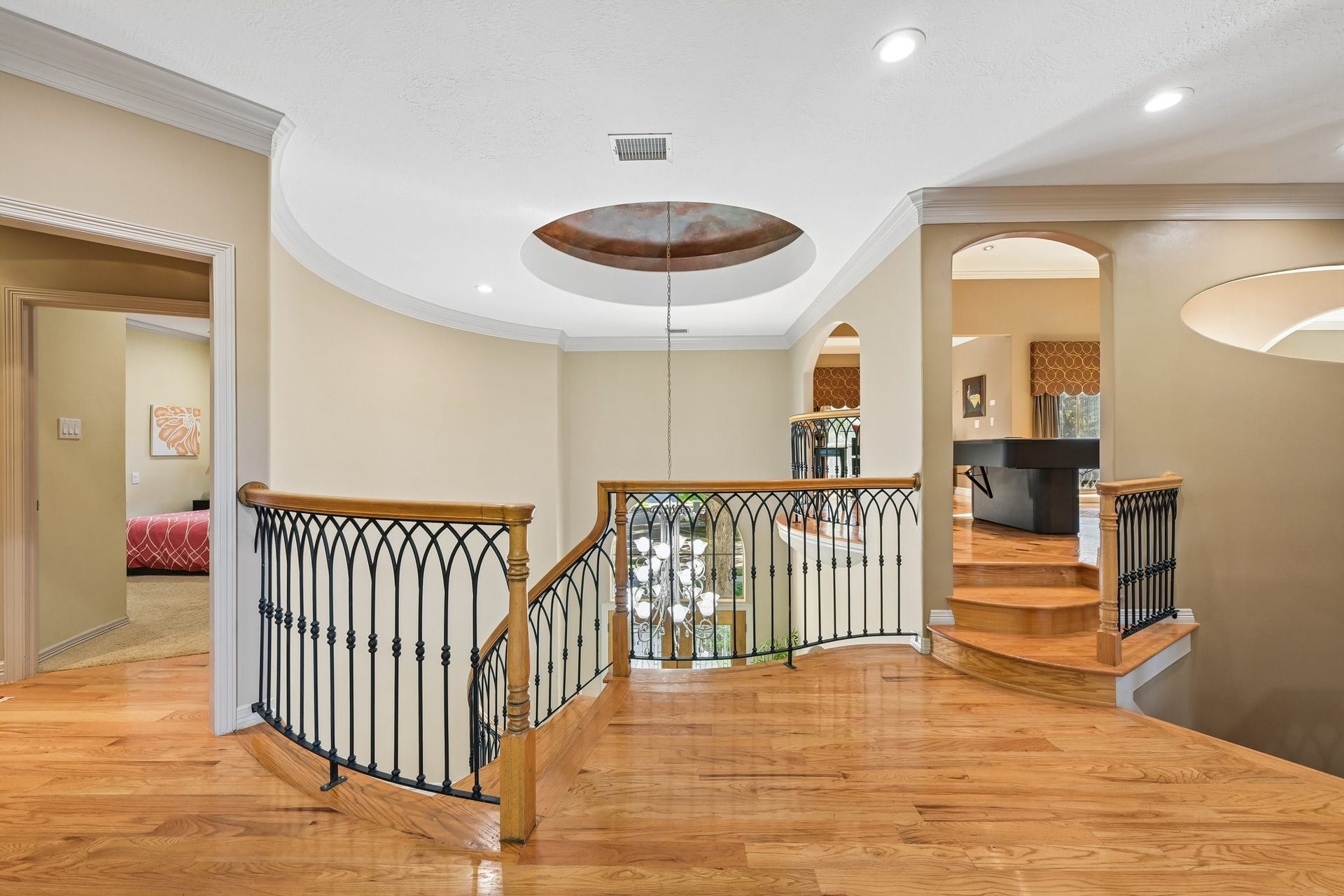 Upstairs landing overlooking the grand two-story foyer, featuring beautiful hardwood flooring, decorative wrought-iron railings, and distinctive architectural ceiling details.