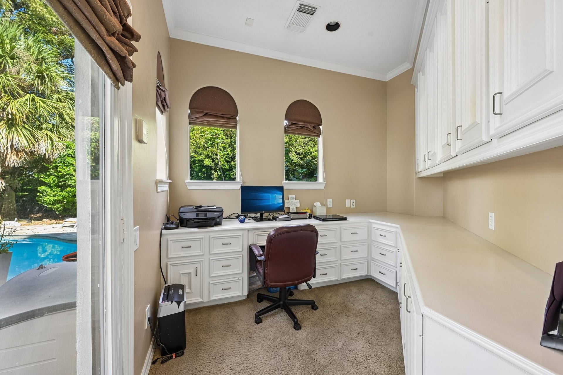 Private study adjoining the primary suite, featuring extensive built-in desk space, abundant cabinetry, and direct access to the pool area