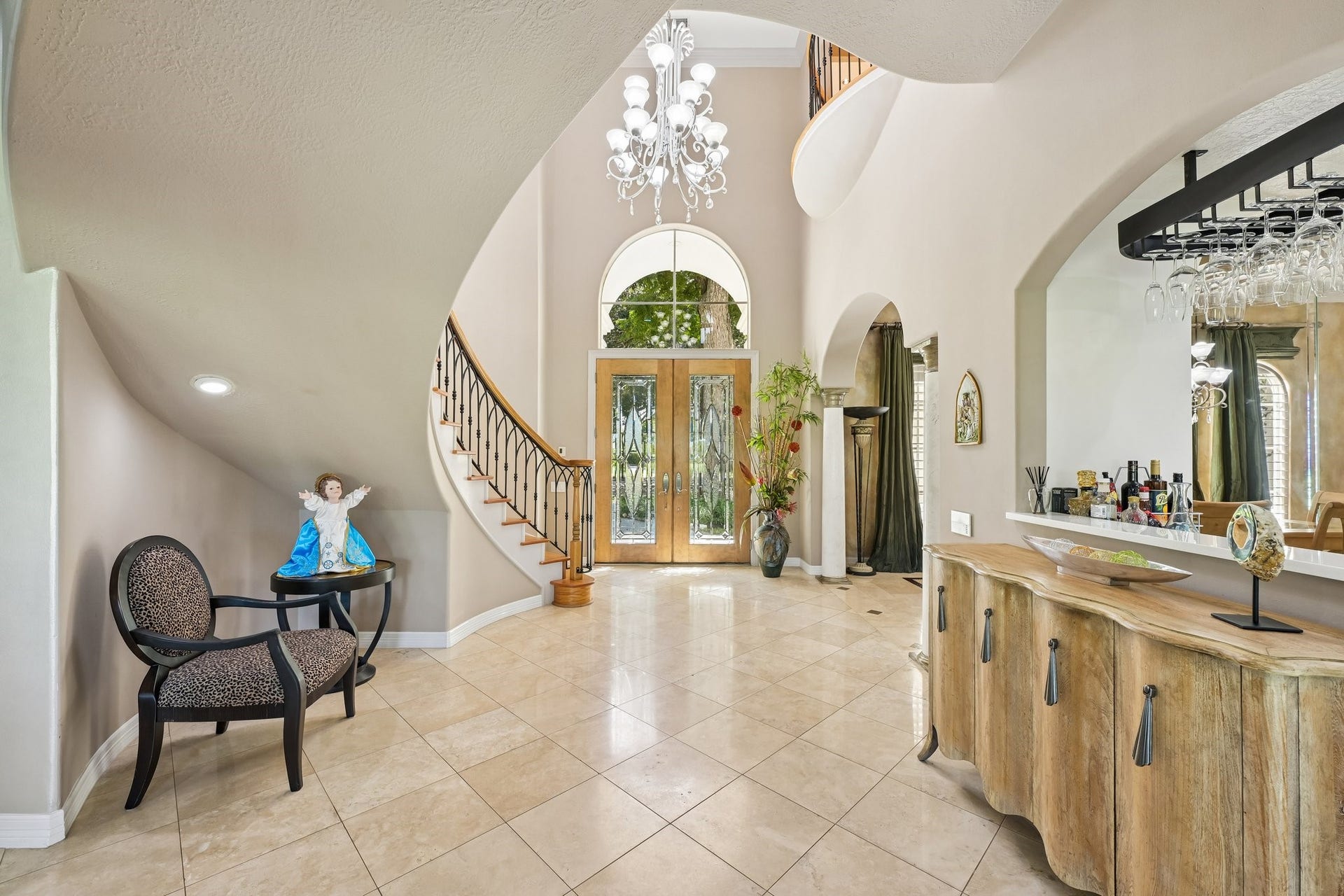 Grand two-story foyer featuring an elegant spiral staircase, arched architectural details, a statement chandelier, and a striking glass-paneled entryway