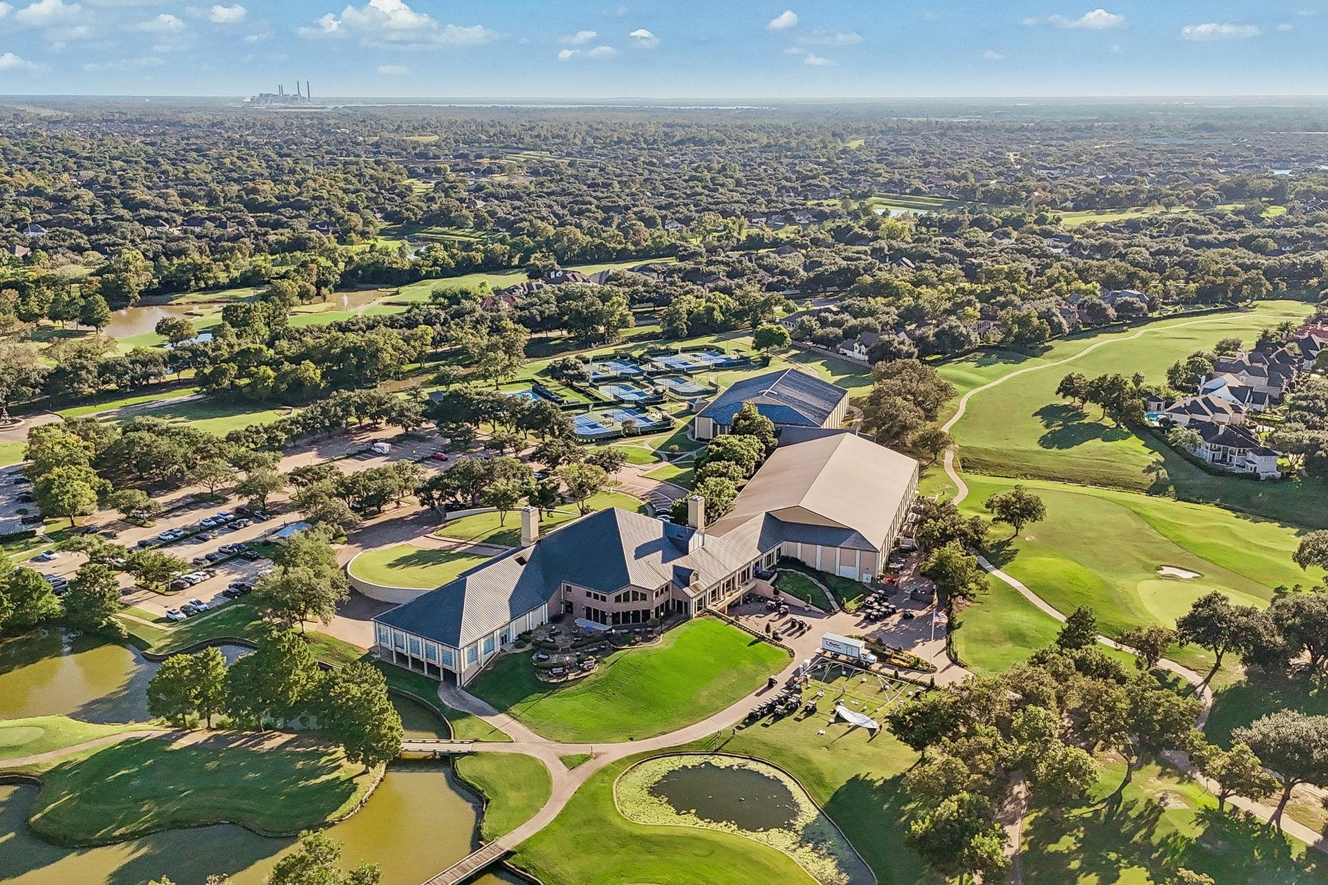 Aerial view of TPC Houstons clubhouse and surrounding grounds, set among manicured golf course greens, water features, and mature landscaping