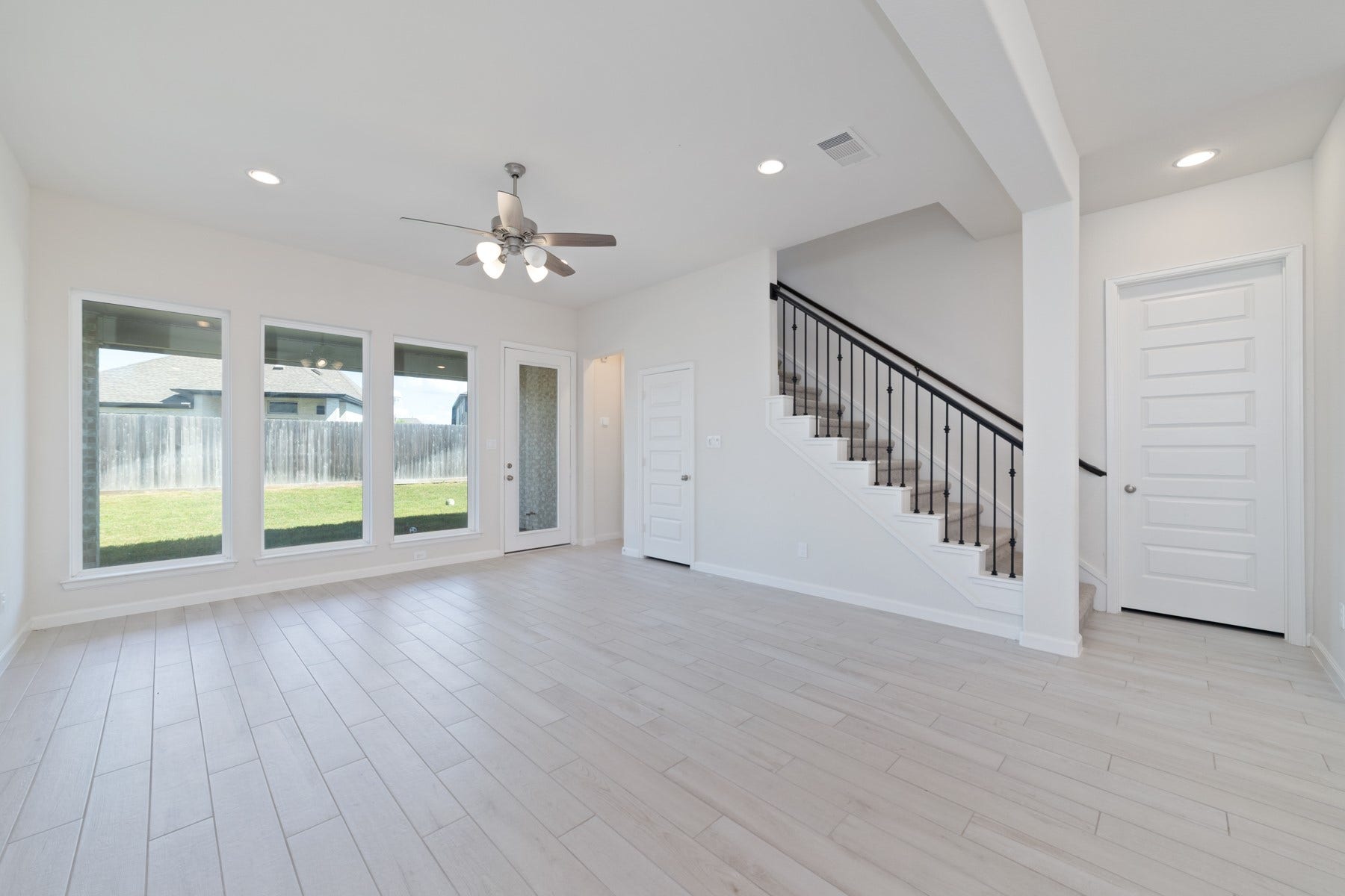 Bright and airy living room with sleek tile floors, large windows offering abundant natural light, and staircase creating a welcoming and modern space.