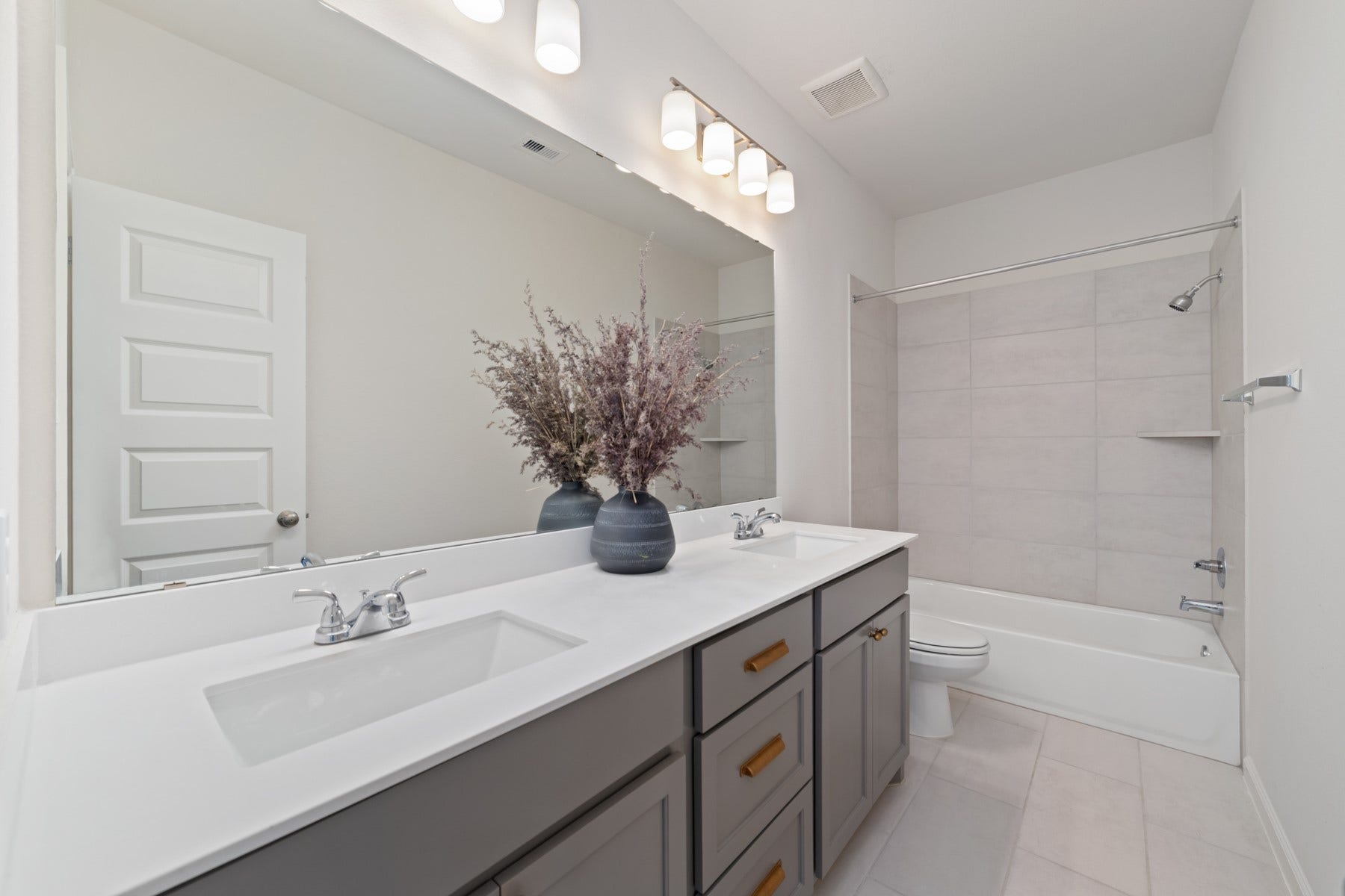 Secondary bathroom featuring a sleek double vanity, ample under-sink storage, and a stylishly tiled shower-tub combo for a luxurious touch.
