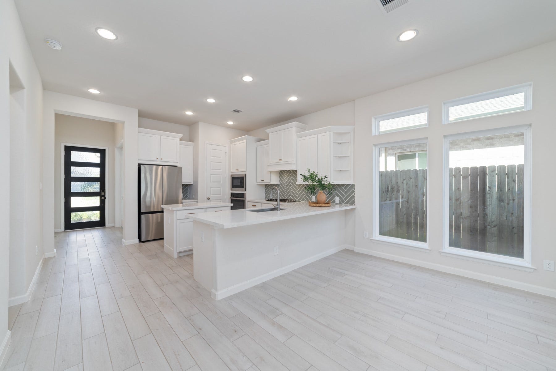 Bright and modern kitchen with sleek stainless steel appliances, elegant white cabinetry, and a spacious island, complemented by large windows for ample natural light.