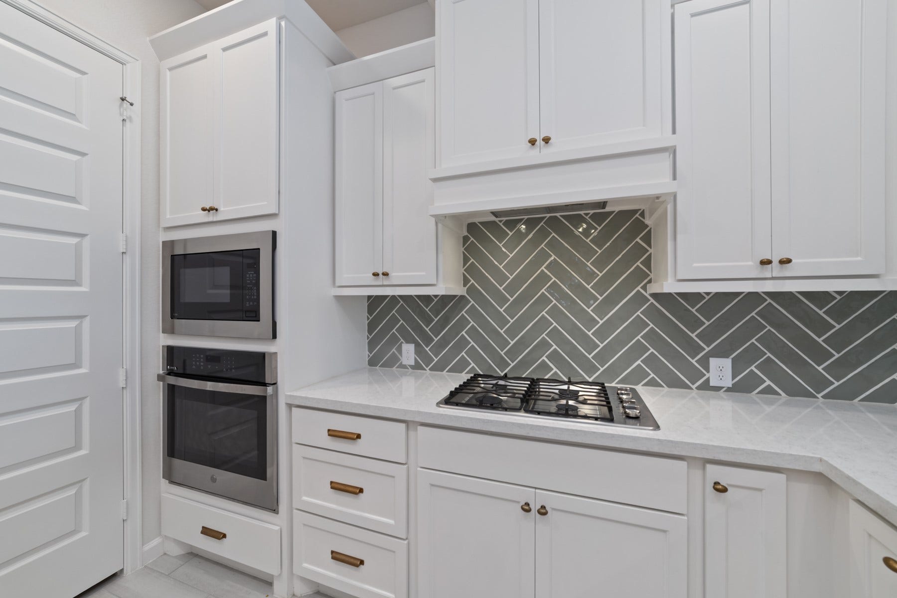 Sleek kitchen featuring a modern gas cooktop, stylish herringbone backsplash, and elegant white cabinetry for a bright, contemporary feel.