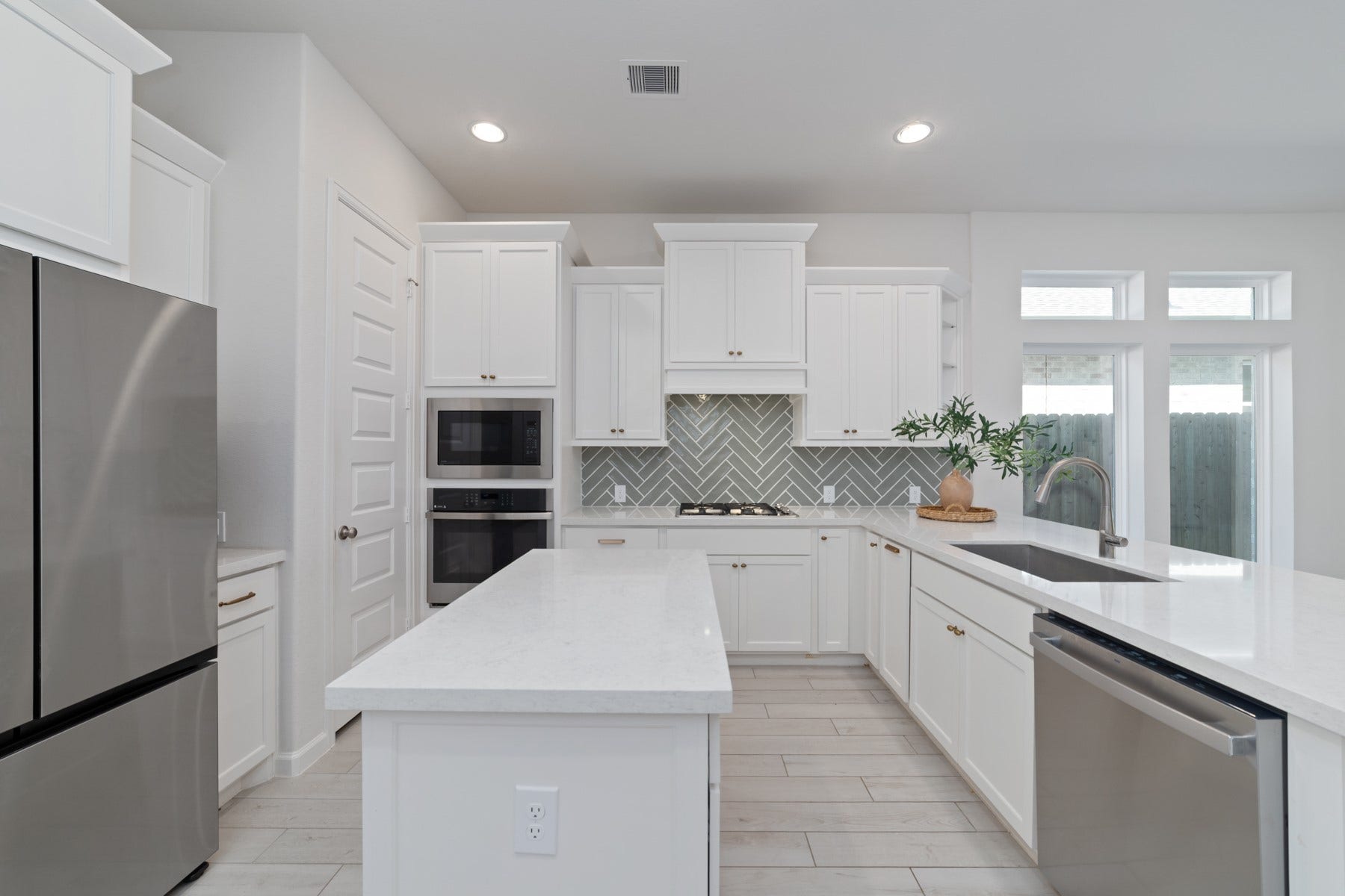 Modern kitchen with sleek white cabinetry, stainless steel appliances, and a stylish herringbone backsplash.