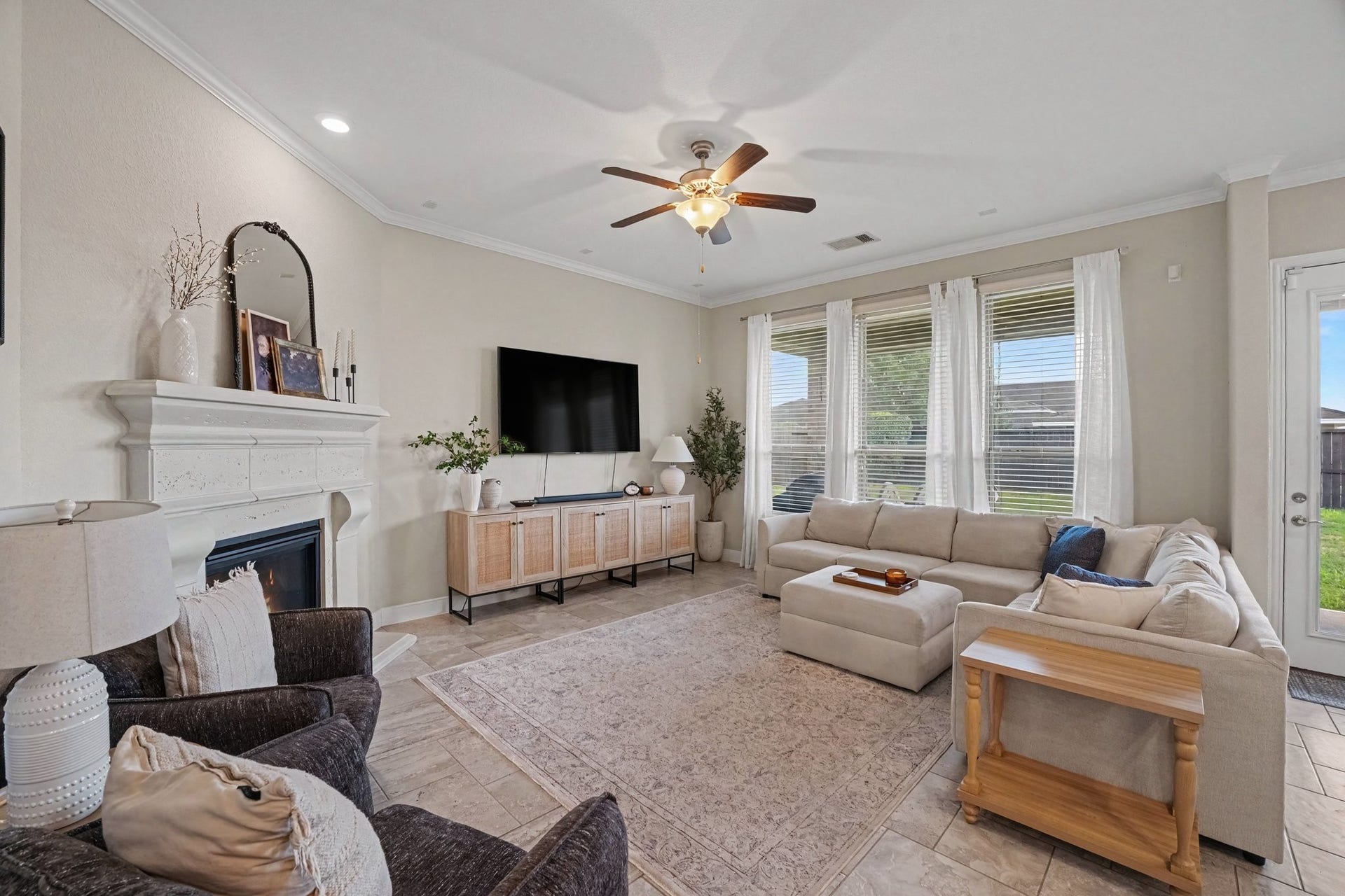 26438 Morgan Creek Lane, Katy, TX 77494 This bright and spacious living room serves as the heart of the home, offering an inviting space designed for both relaxation and entertaining. High ceilings with crown molding, recessed lighting, and a classical wooden ceiling fan set a airy, elevated tone. Wall-to-wall windows topped with sheer drapes flood the room with natural light while providing views out to the backyard.