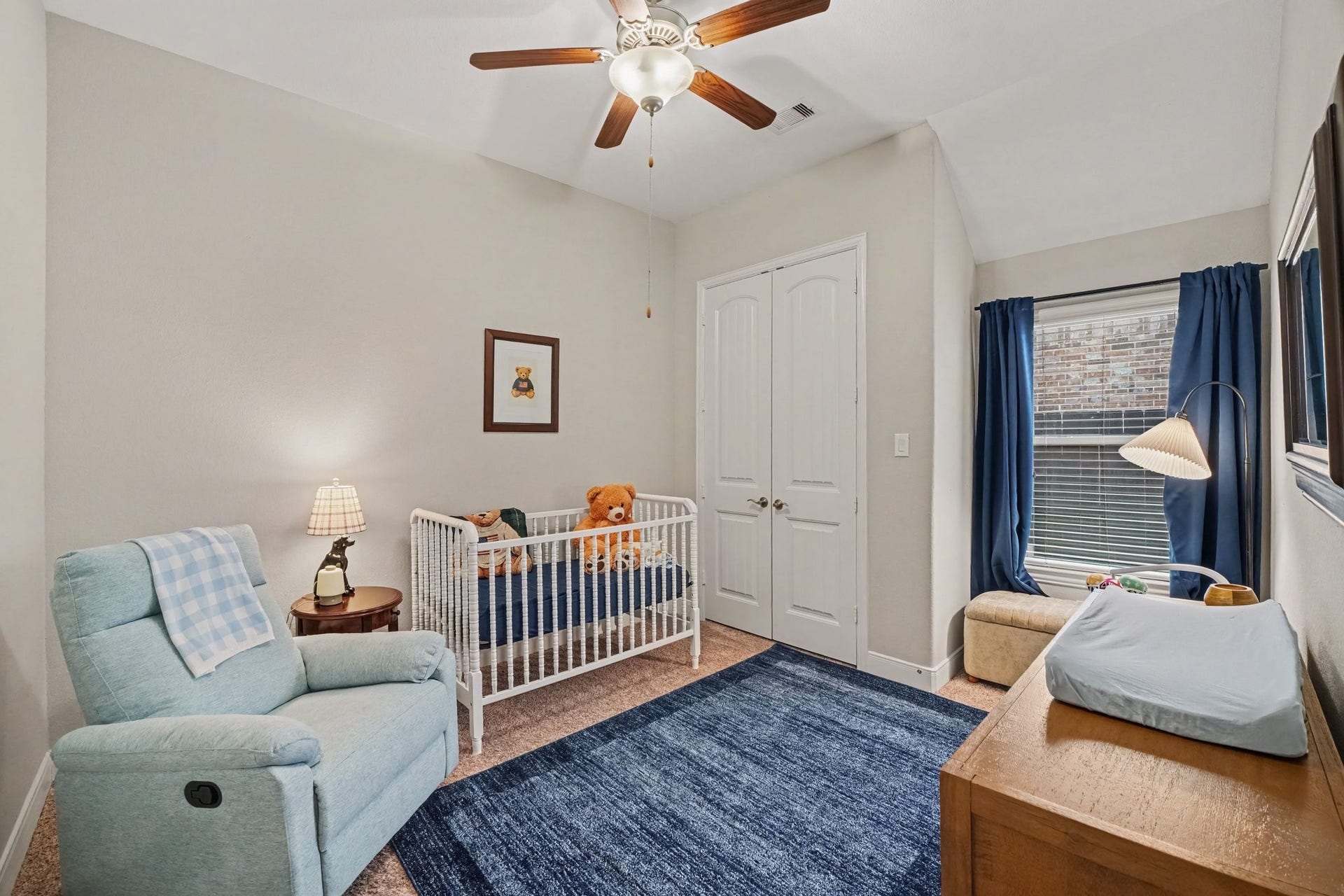 26438 Morgan Creek Lane, Katy, TX 77494 This inviting secondary bedroom, currently outfitted as a cozy nursery, features vaulted ceilings that add an airy and spacious feel to the room. A classic wooden ceiling fan with an integrated light fixture anchors the top of the space, while neutral grey walls and plush carpeting create a comfortable environment underfoot.