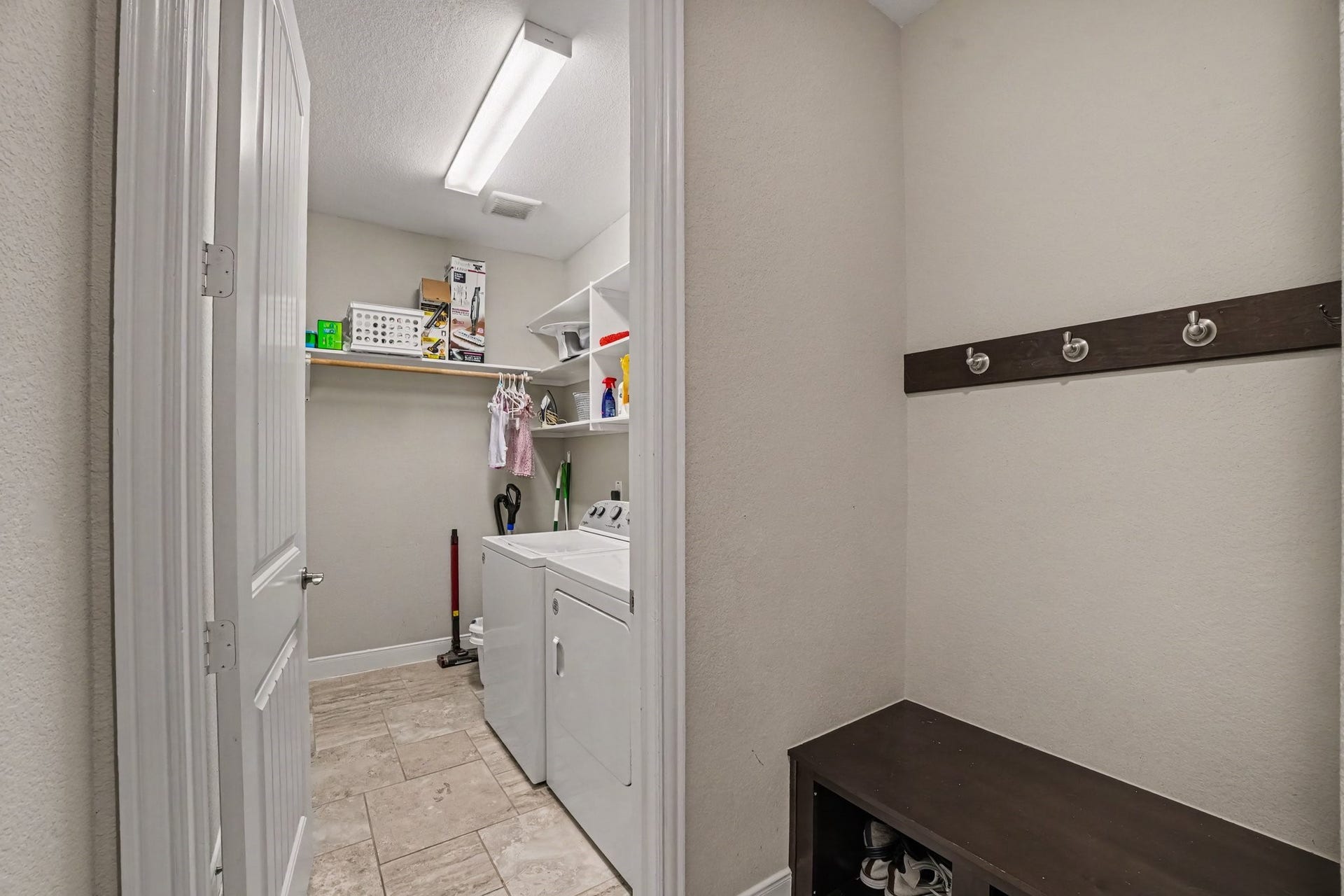 26438 Morgan Creek Lane, Katy, TX 77494 This dedicated utility hub highlights everyday convenience with a functional laundry room and mudroom entry drop zone. Right outside the laundry door, a dark wood bench with shoe storage cubbies and a wall-mounted hook rail provides the perfect spot to kick off shoes and hang coats or bags. Stepping through the doorway reveals a spacious laundry room equipped with a side-by-side washer and dryer.