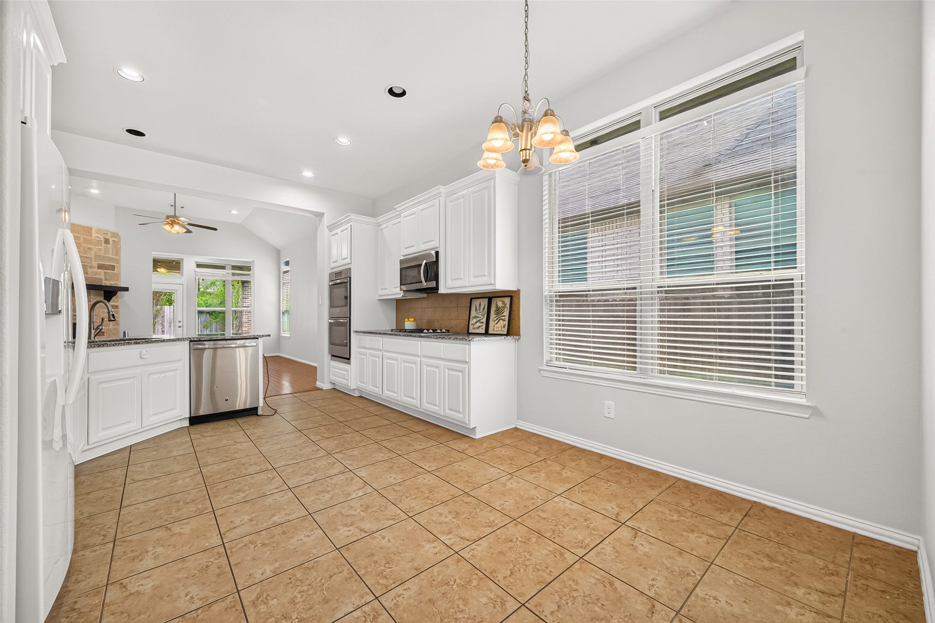 8155 Laughing Falcon Trail, Conroe, TX 77385 Bright kitchen and adjoining breakfast area with white cabinetry, abundant windows, tile flooring, and pendant lighting.