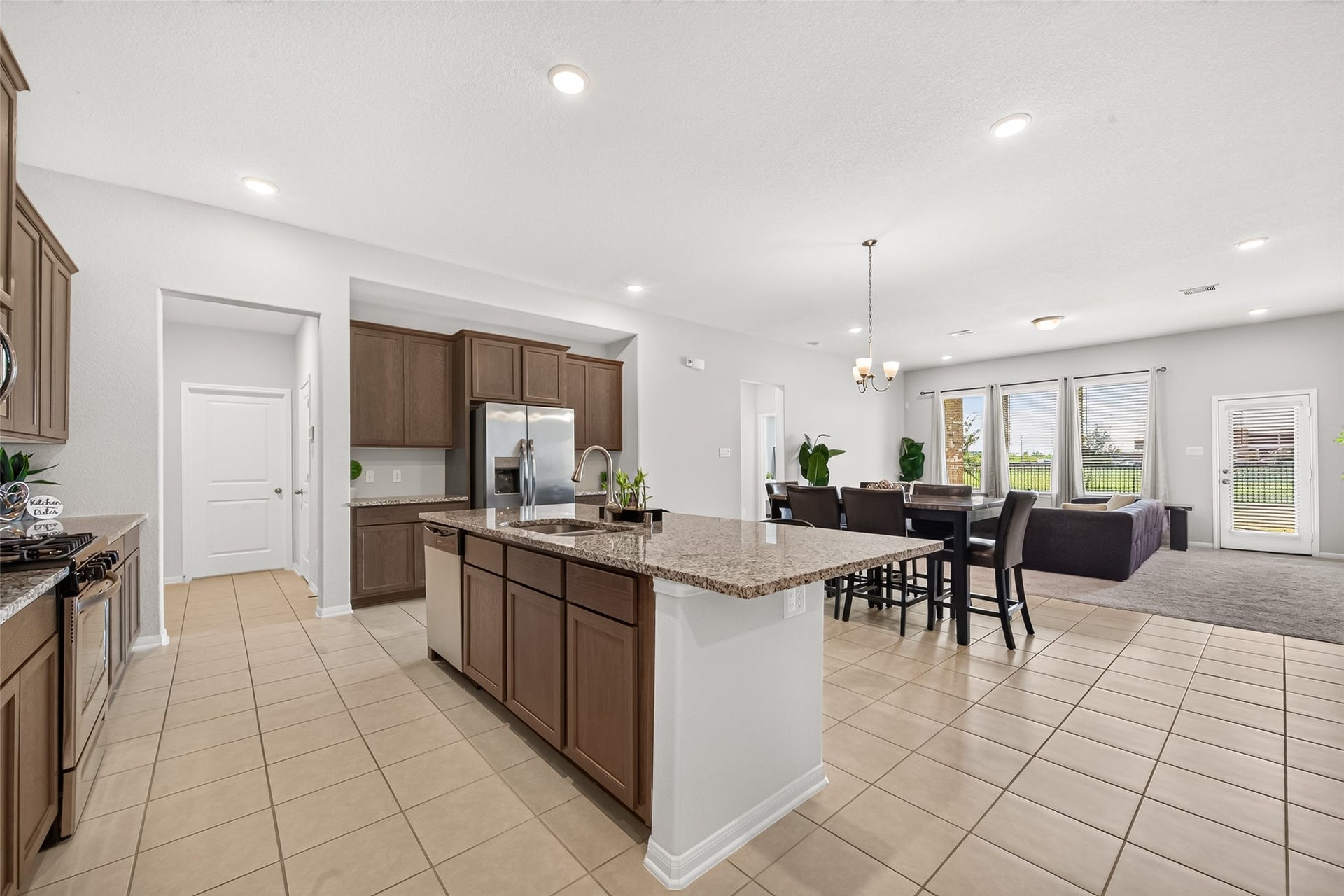 10707 Amador Peak Drive, Rosharon, TX 77583 Kitchen island includes large double sink, kitchen open to living room, utility room, walk-in pantry, & garage access on left side of photo, primary bedroom through door straight ahead. Great view of the backyard and scenery.