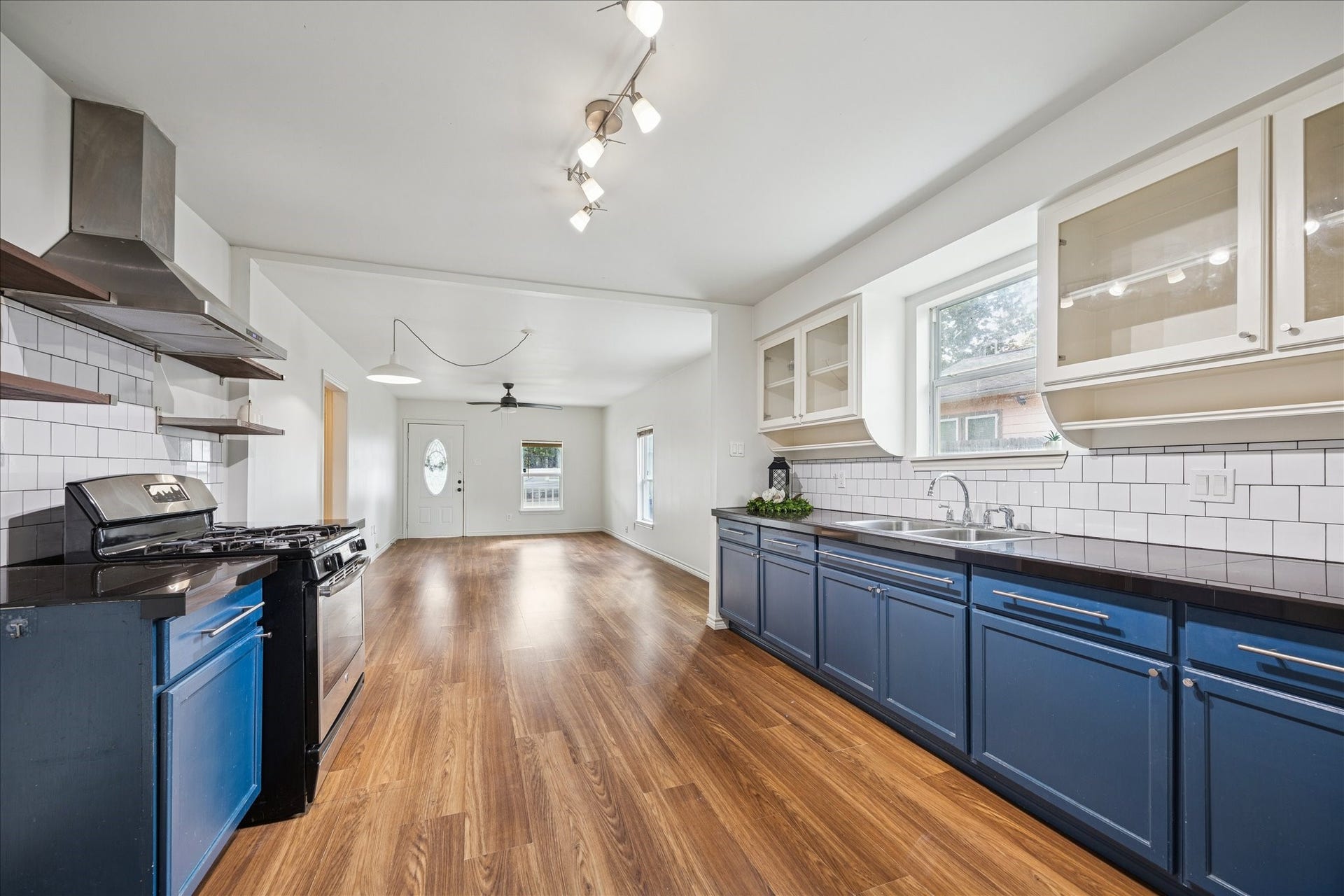 7933 Elwood Street, Houston, TX 77012 This photo showcases a bright and spacious kitchen with modern amenities, featuring blue lower cabinets, white tile backsplash, and a sleek stainless steel stove. The open layout extends into a living area ample natural light.