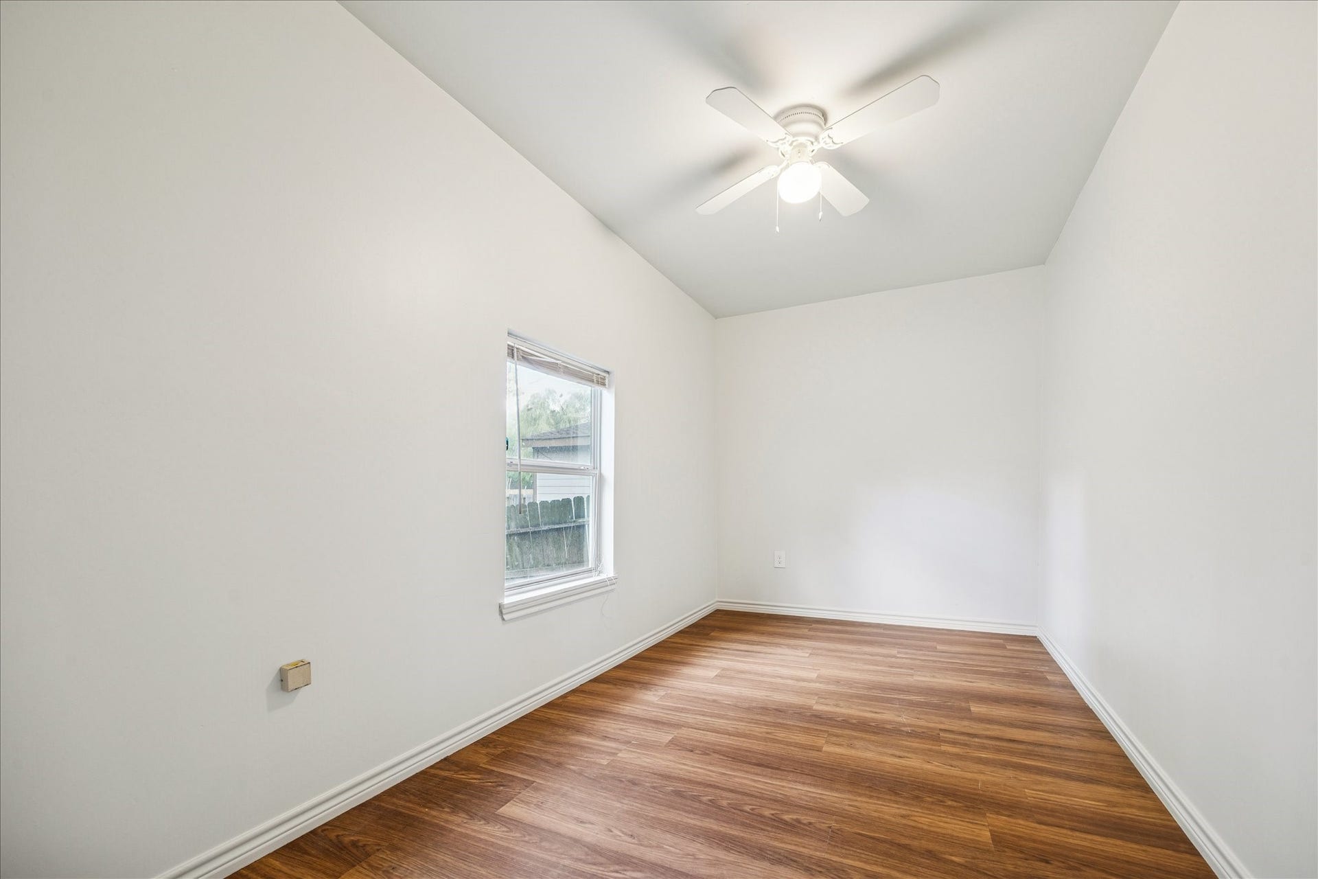 7933 Elwood Street, Houston, TX 77012 Bright room with white walls, vinyl wood flooring, and a ceiling fan. It has a single window allowing natural light. Ideal for a home office or cozy bedroom.