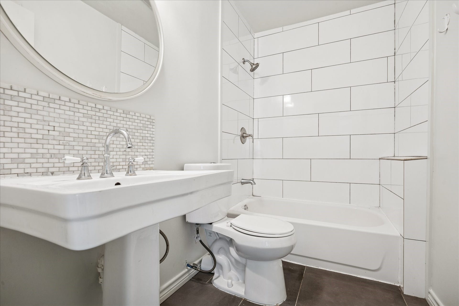 7933 Elwood Street, Houston, TX 77012 This bathroom features a modern design with a white subway tile shower, a sleek pedestal sink, and a large round mirror. The mosaic tile backsplash adds a stylish touch, while the neutral color palette creates a bright and clean atmosphere.