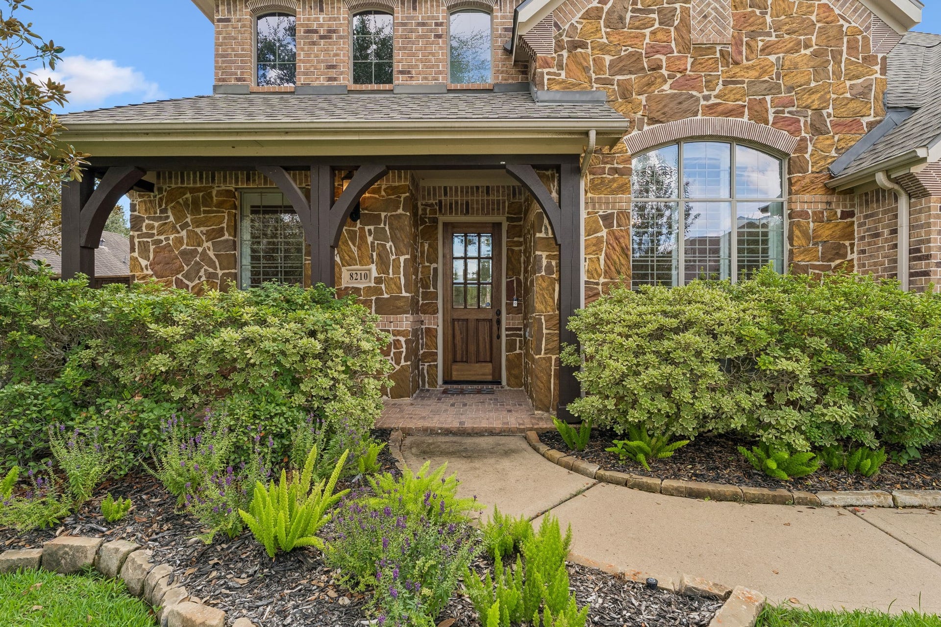 8210 Thunder Ridge Way, Missouri City, TX 77459 Charming stone facade with an inviting curved sidewalk leading from the driveway, surrounded by lush greenery.