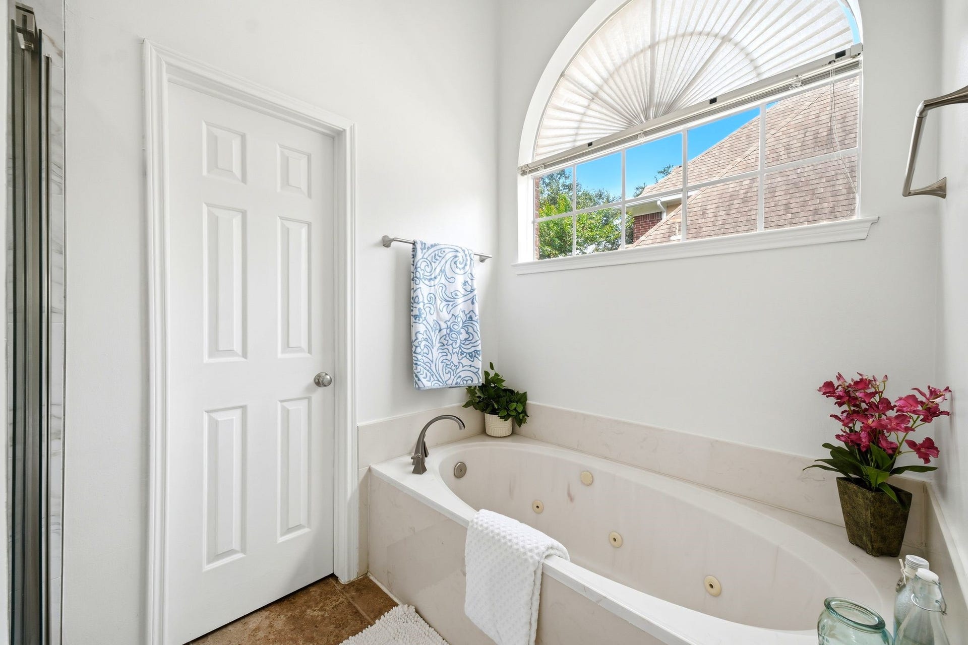 2216 Fairwater Park Drive, League City, TX 77573 Experience serene luxury in this bright bathroom, featuring a jetted bathtub beneath an arched window, enhanced by elegant fixtures and lush decorative plants.