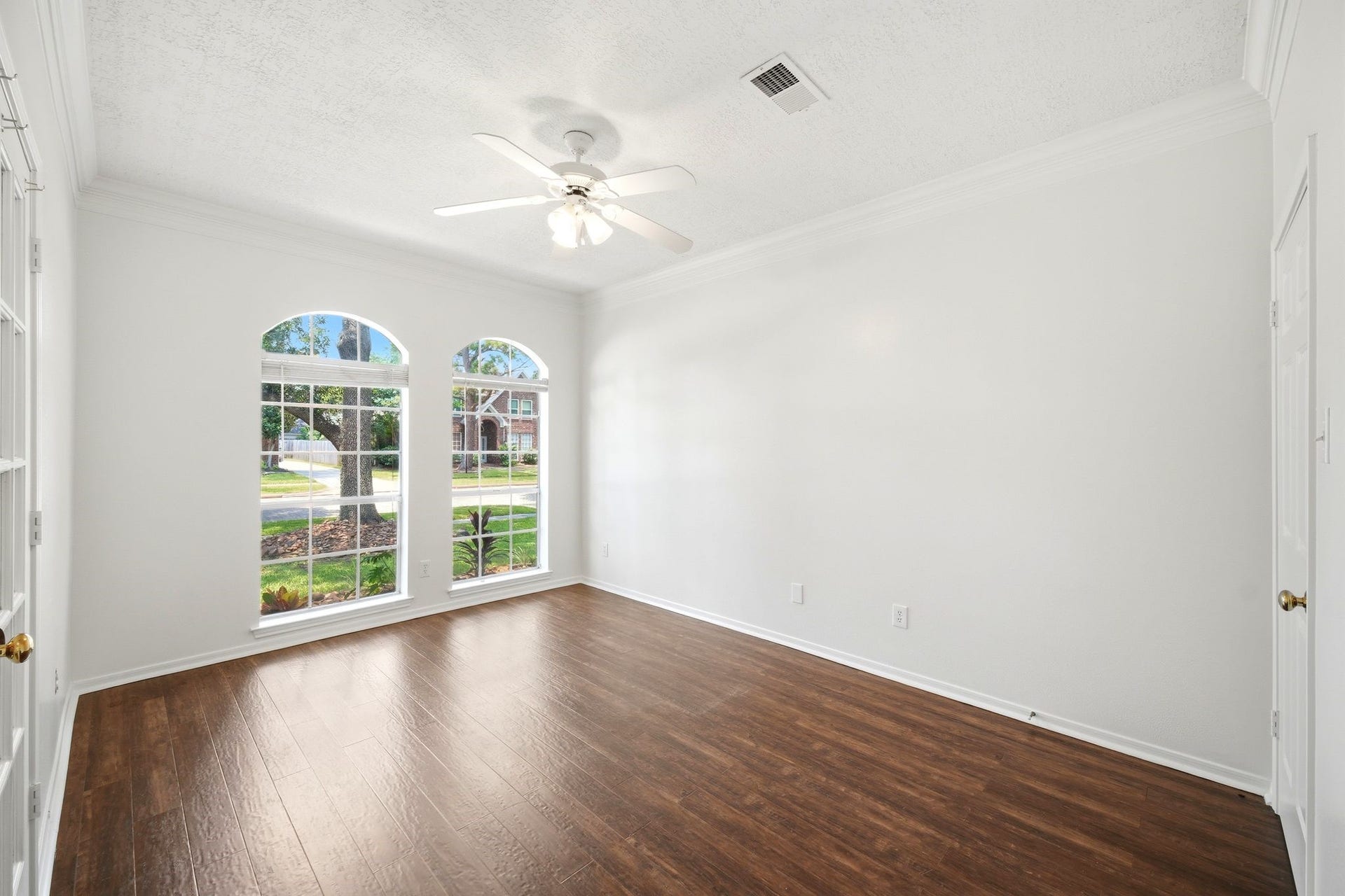 2216 Fairwater Park Drive, League City, TX 77573 Bright and inviting, this unstaged home office features elegant wood flooring and large arched windows that flood the space with natural light, offering a serene and productive environment.
