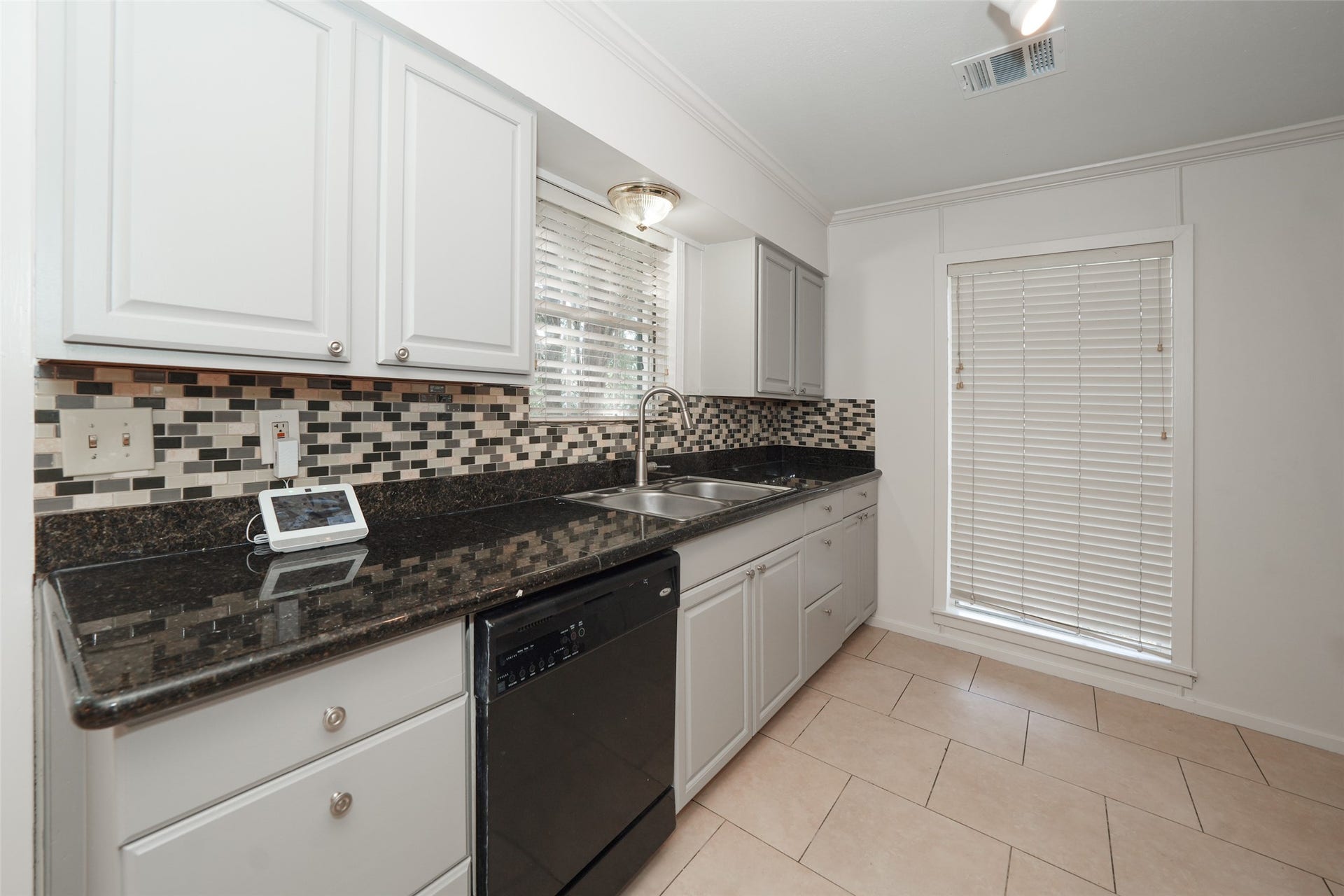 9519 Val Verde Street, Houston, TX 77063 Modern kitchen with sleek granite countertops, mosaic tile backsplash, and light cabinetry. Includes a double sink, black dishwasher, and ample natural light through a window with blinds.