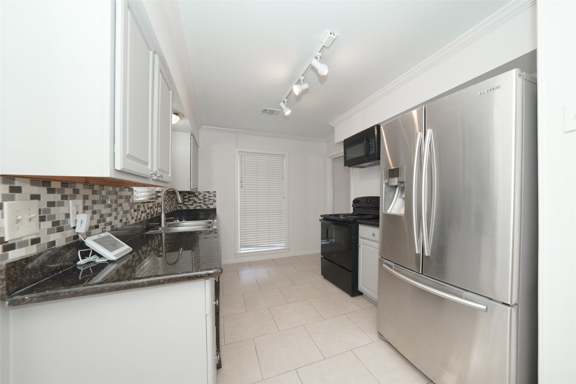 9519 Val Verde Street, Houston, TX 77063 This modern kitchen features sleek stainless steel appliances, granite countertops, and a stylish tile backsplash. It offers ample cabinet space and natural light, creating a bright and functional cooking area.