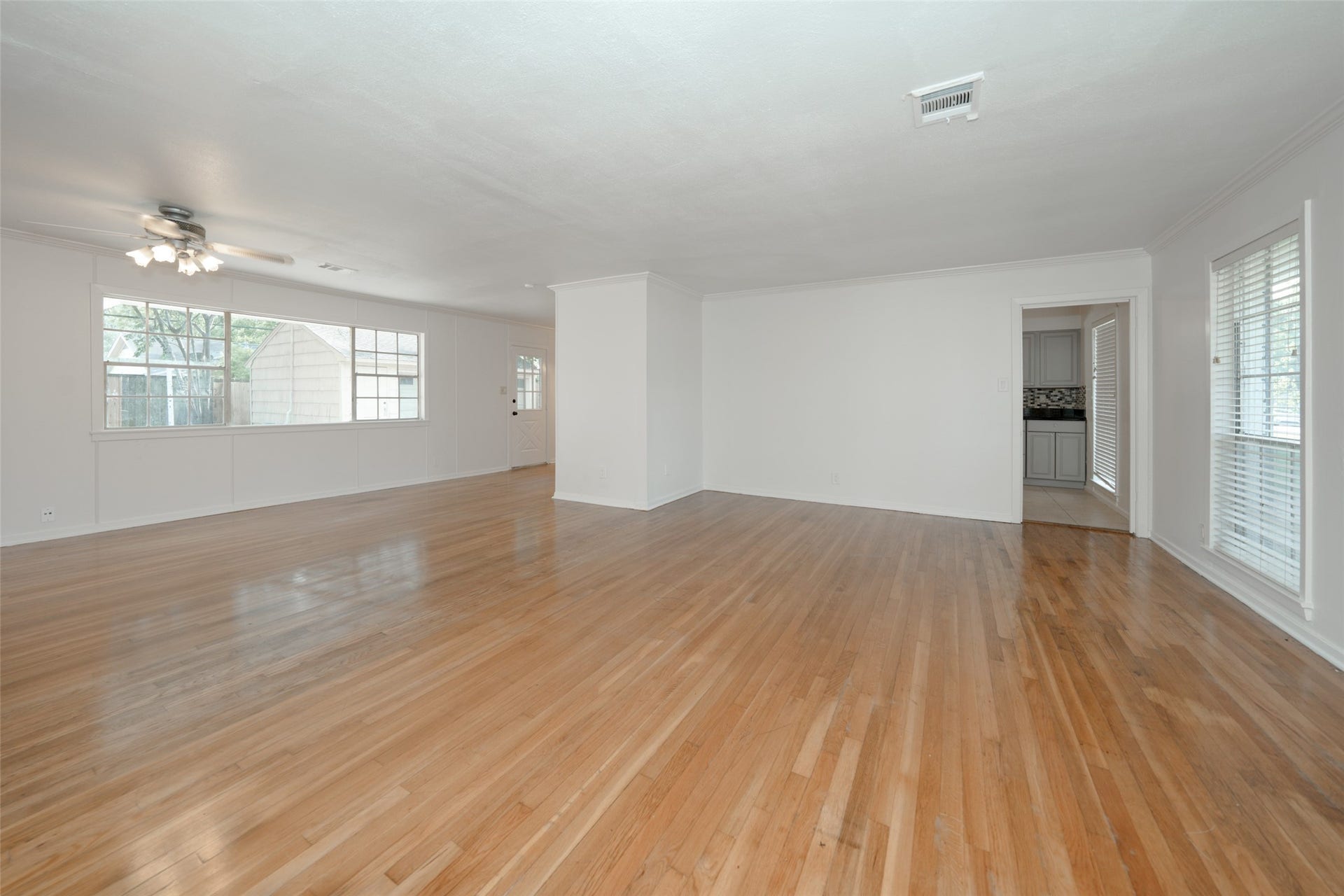 9519 Val Verde Street, Houston, TX 77063 Spacious, light-filled living area with polished hardwood floors, large windows, and a ceiling fan. The open layout leads to an adjacent room, perfect for versatile use.